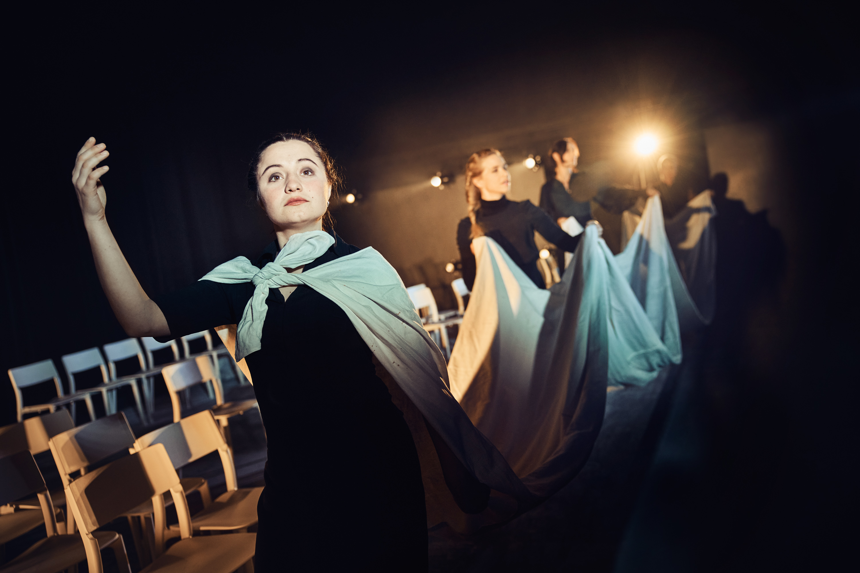 En kvinde i sort med hvidt stof bundet om skuldrene som langt slæb, som 3 andre kvinder holder. Fra forestilling Kvinde kend din historie på Odense Teater