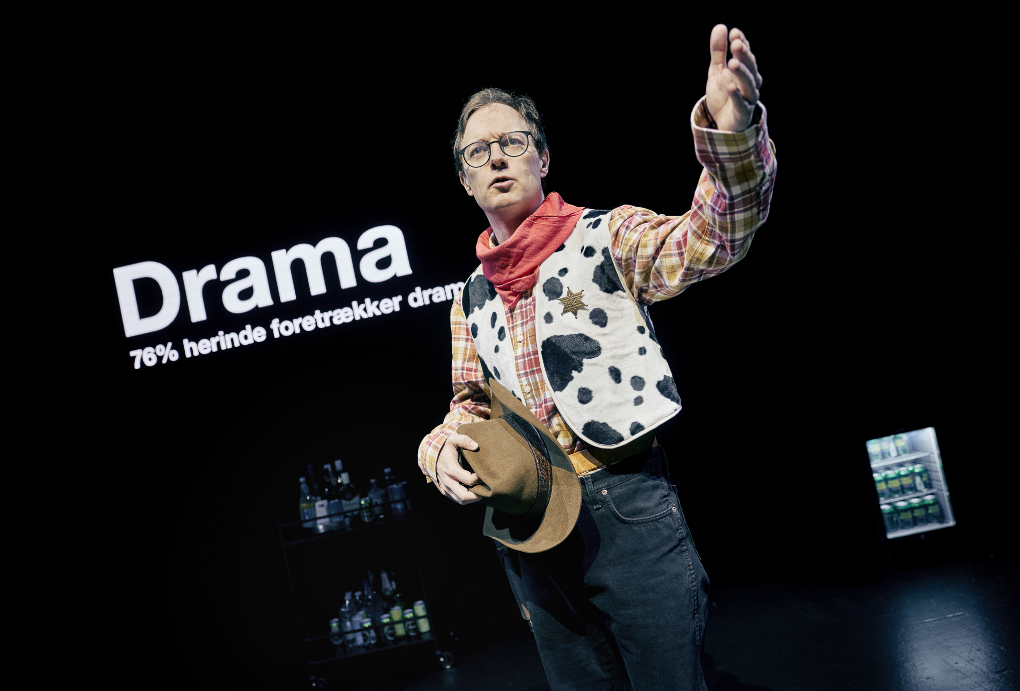 En mand i cowboytøj og en cowboyhat i hånden står på en sort sene. Fra forestillingen AI know you på Odense Teater