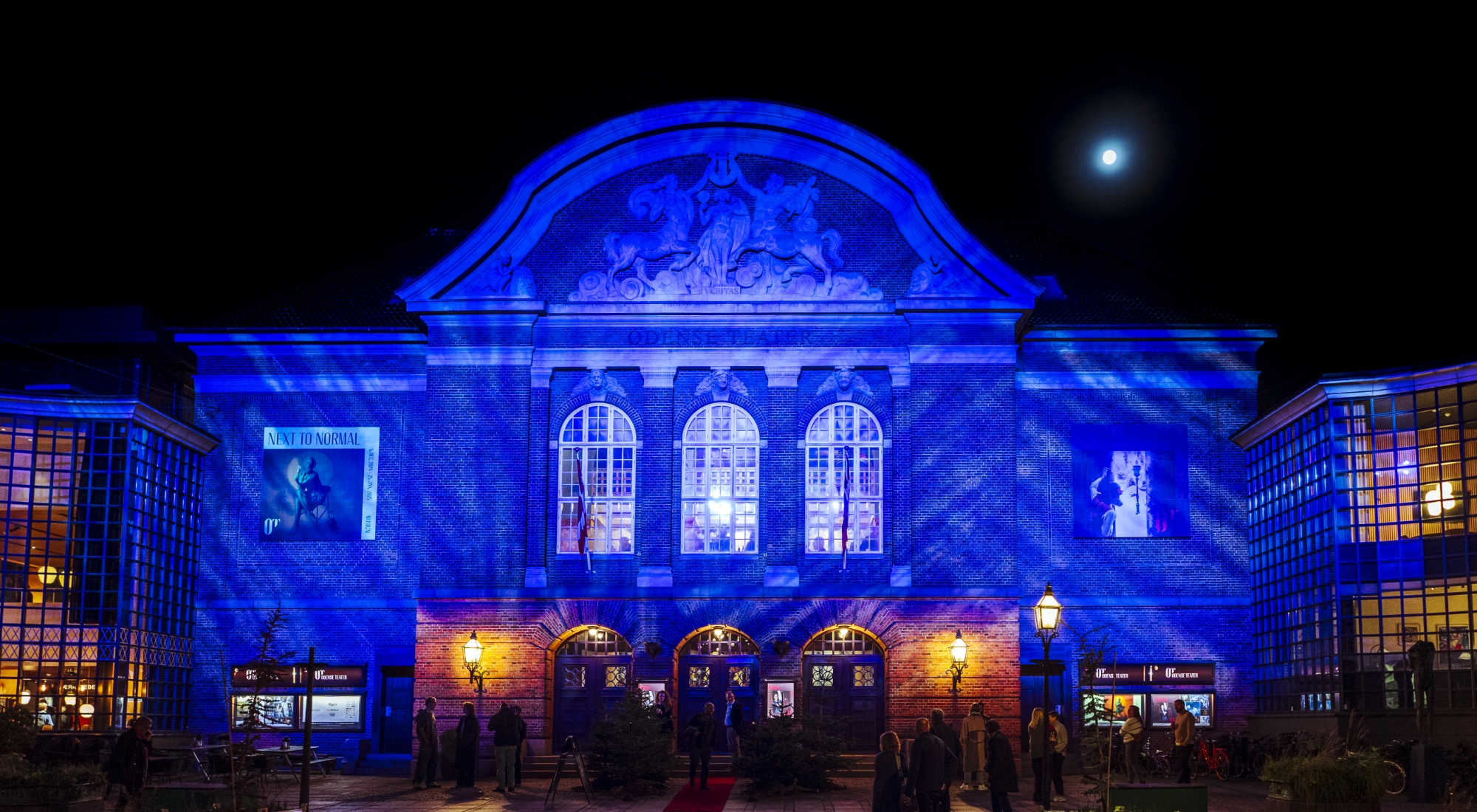 Facade Odense Teater i aftenlys. Oplyst af blåt lys og med månen på den sorte himmel.