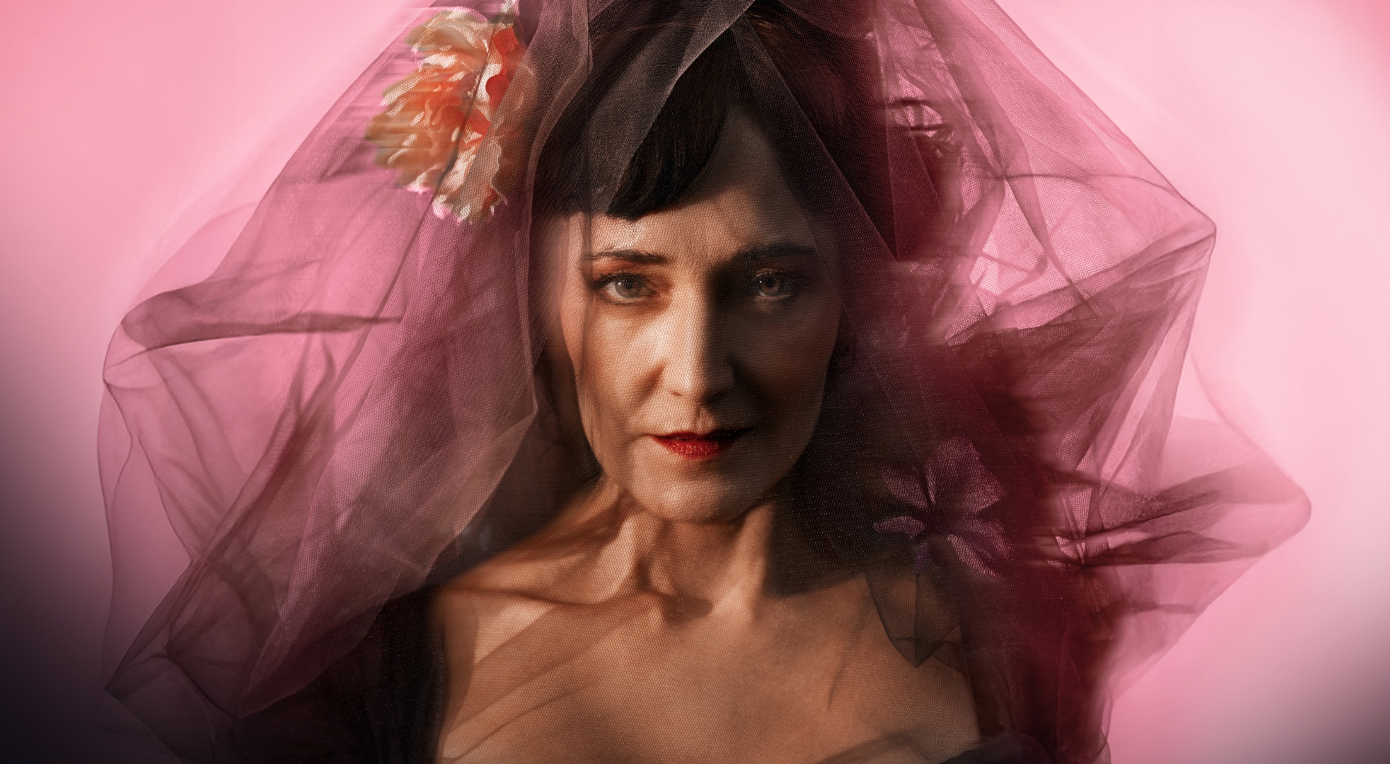 Portræt af mørkhåret kvinde med sort slør og en blomst i siden. Pink baggrund. Fra forestillingen Fru Marie Grubbe på Odense Teater