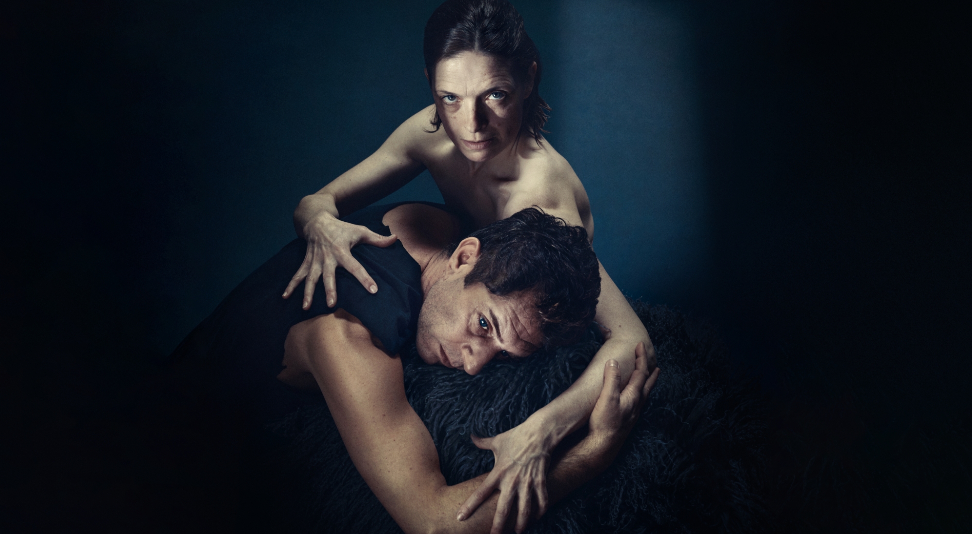 En kvinde med nøgen overkrop stirrer vagtsomt i kameraet, på hendes skød ligger en mørkhåret mand . Han ser ikke i kamera. Fra forestillingen Når vi døde vågner på Odense Teater