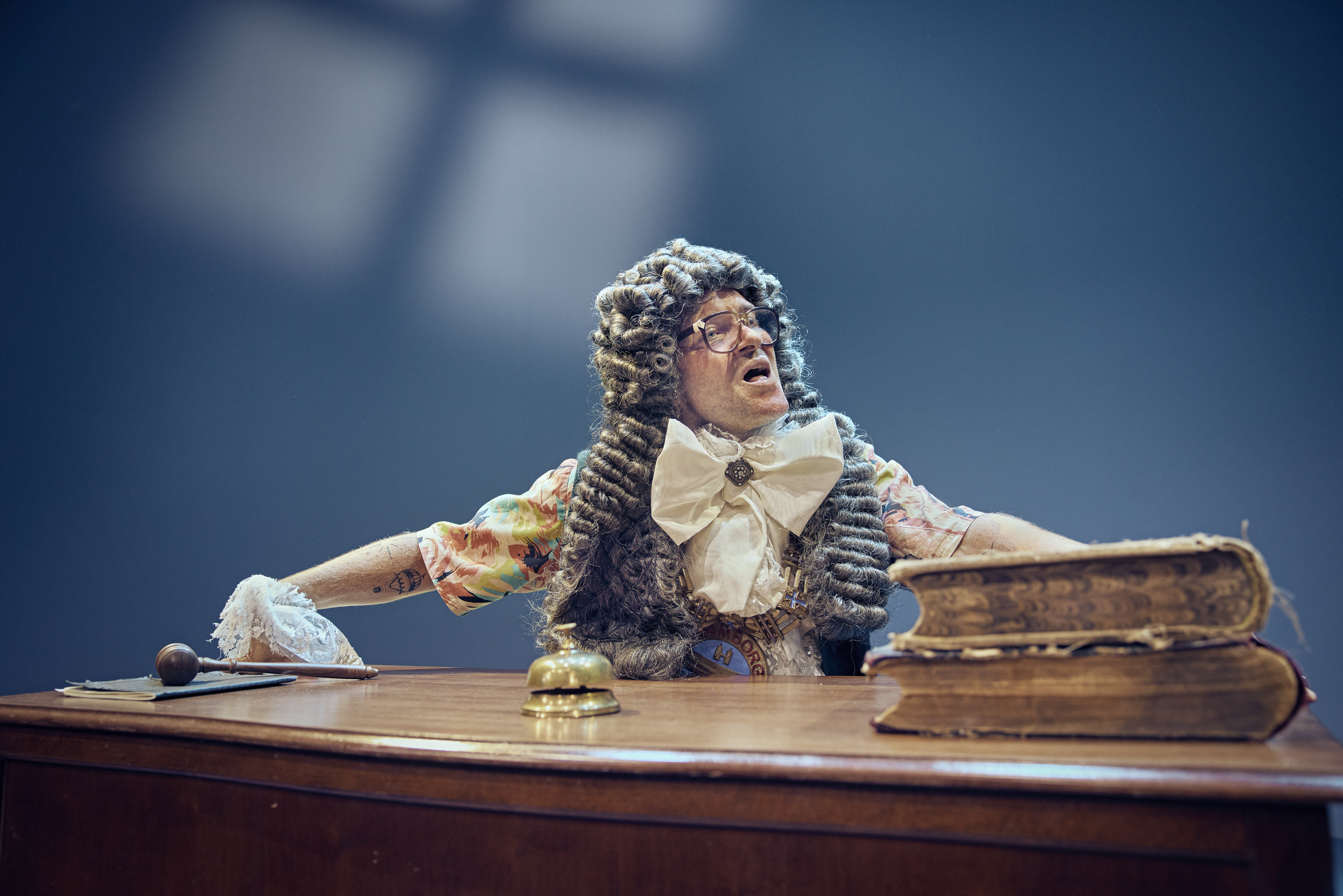 En mand med stor krøllet paryk fra 1700 tallet sidder ved skrivebord. Fra teaterforestillingen Den politiske kandestøber på Odense Teater