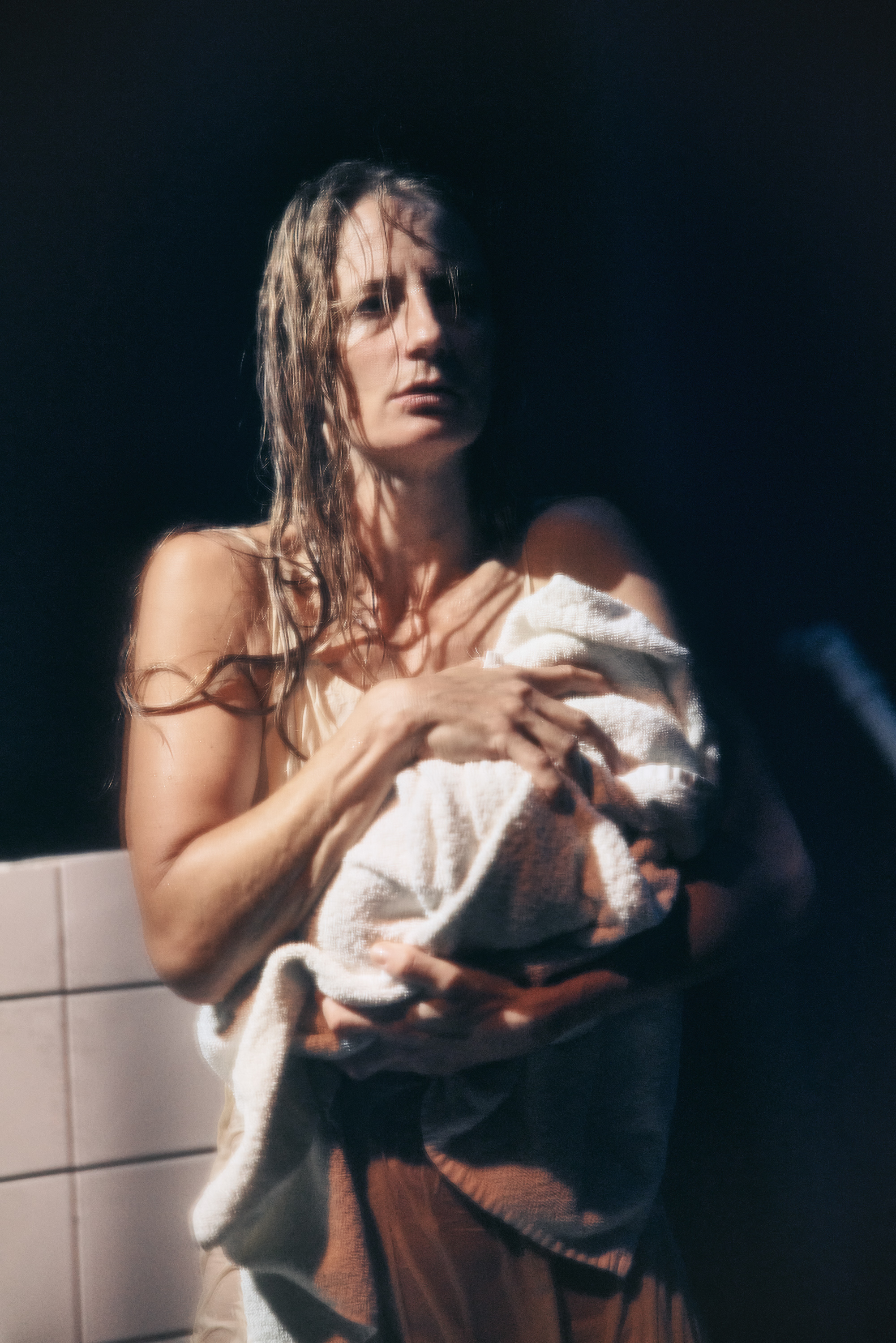 En våd kvinde med langt hår, står med et spædbarn svøbt i et håndklæde i armene. Fra forestillingen Fruen fra havet på Odesense Teater. 