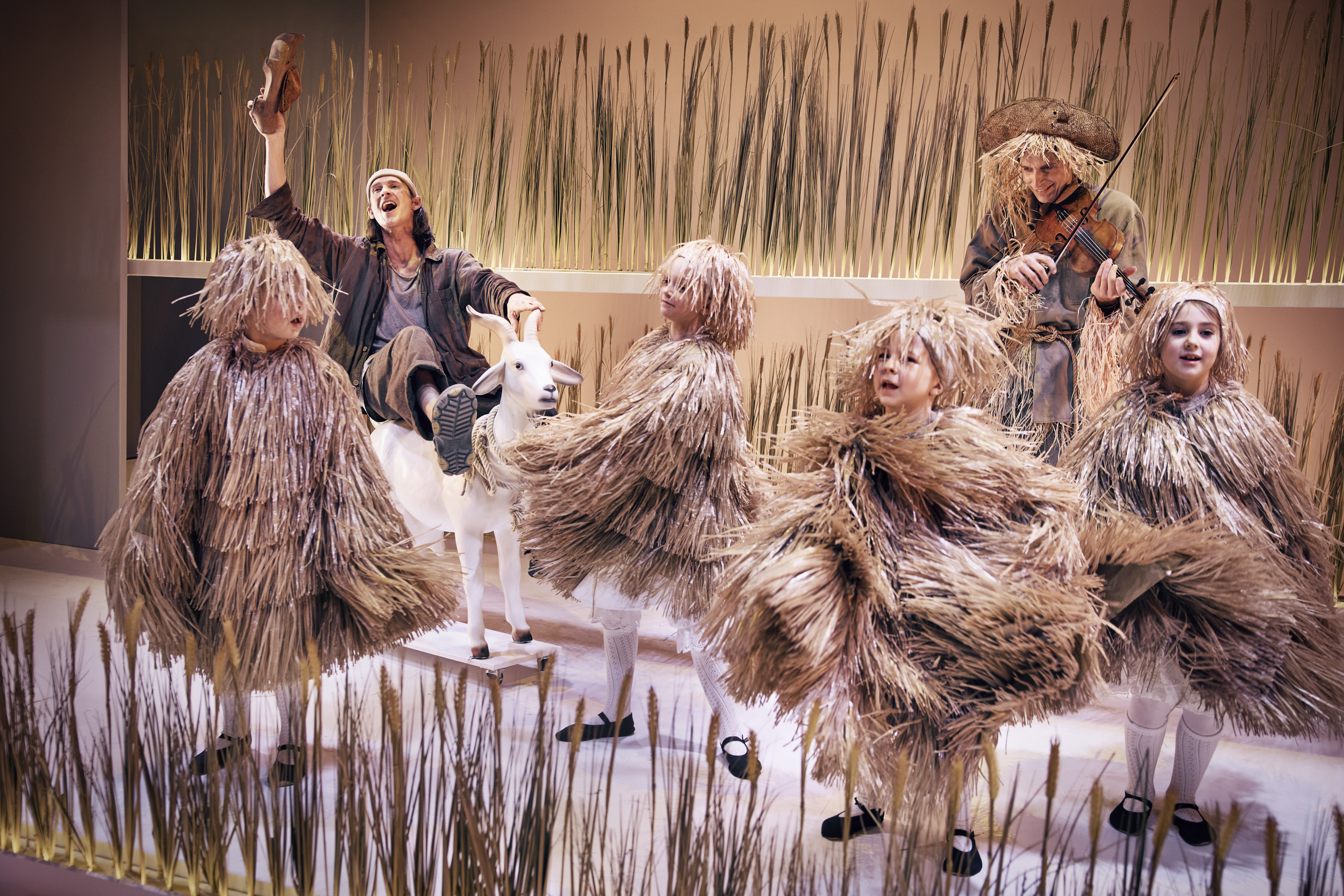 Klodshans ridder på sin ged mens børn klædt ud som høstakke danser og fugleskræmsel spiller violin. Fra Teaterforestilling Klodshans på Odense Teater
