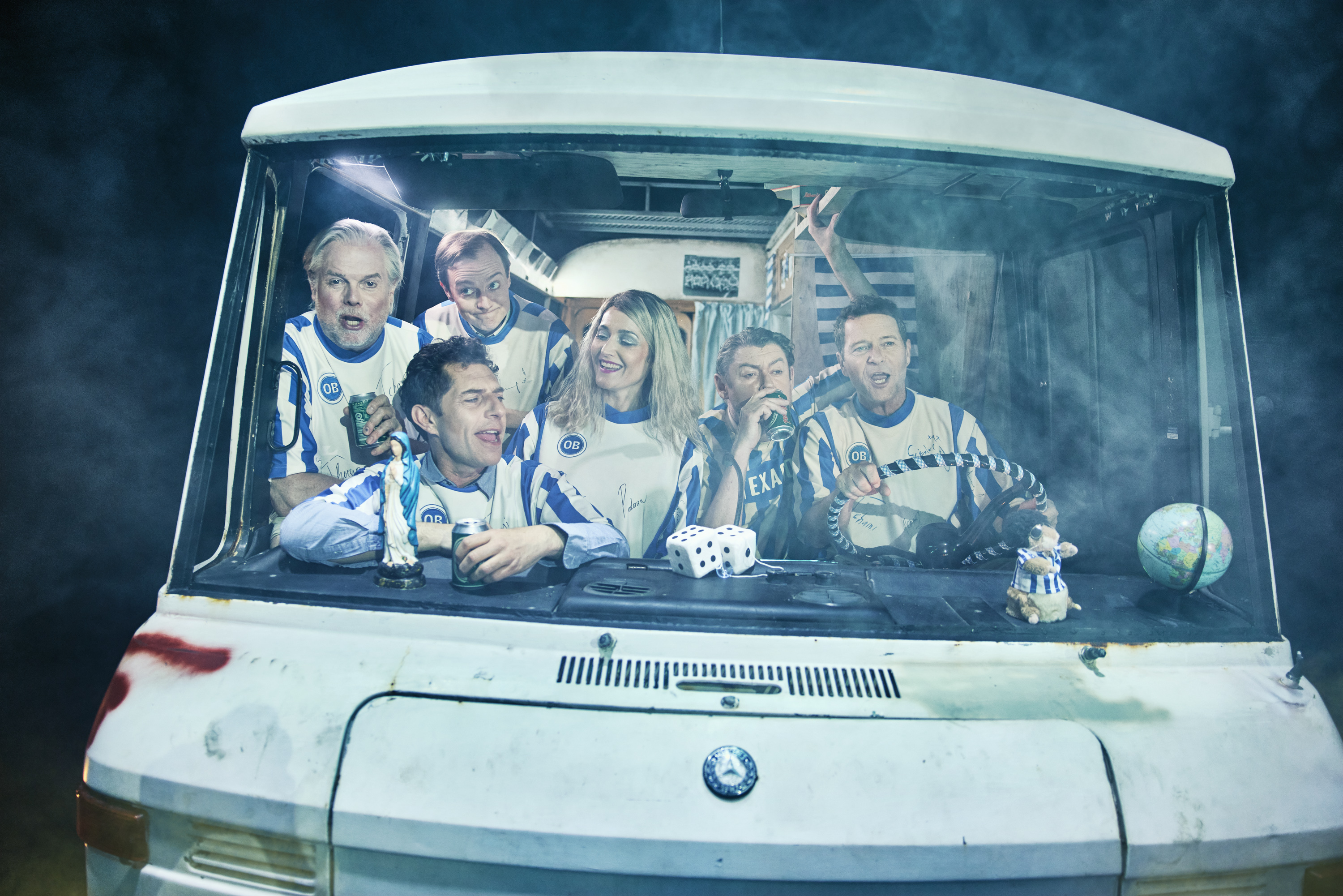 seks mennesker sidder i en gammel autocamper. De har alle OB fodboldtrøjer på . Fra teaterforestillingen Miraklet i Madrid på Odense Teater