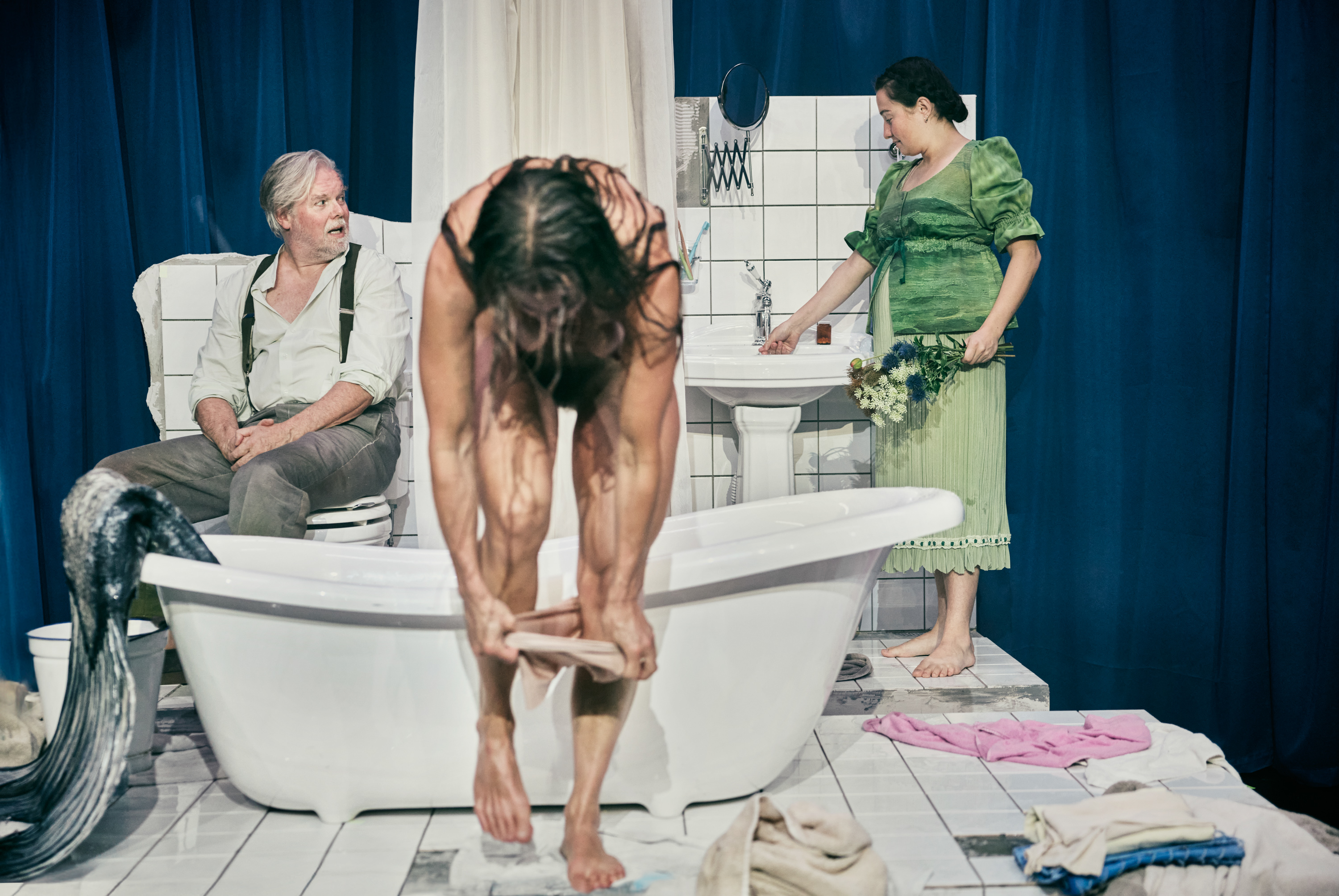 Scene fra forestillingen Fruen fra havet på Odesense Teater. Et badeværelse. En nøgen kvinde er ved at tage undertøj på. I baggrunden en kvinde og en mand.