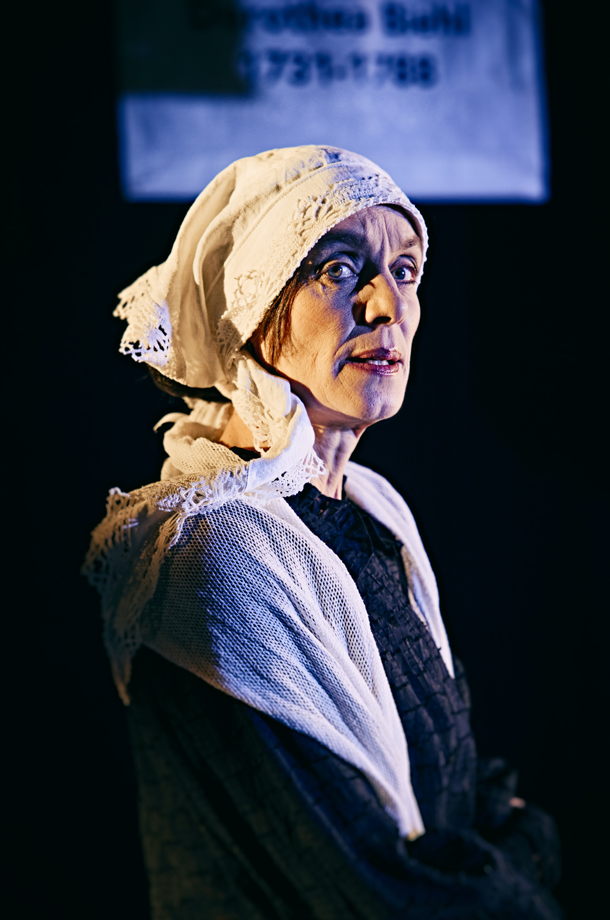 Portræt af en kvinde klædt i sort med hvidt sjal og tørklæde om hovedet. Fra forestilling Kvinde kend din historie på Odense Teater