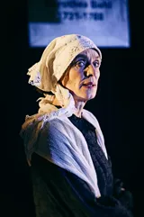 Portræt af en kvinde klædt i sort med hvidt sjal og tørklæde om hovedet. Fra forestilling Kvinde kend din historie på Odense Teater