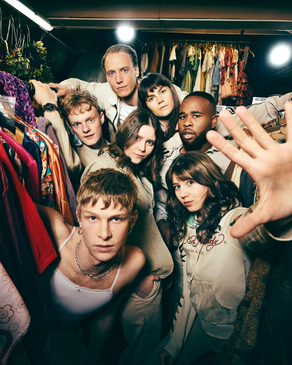 7 Unge mennesker der står imellem stativer med tøj på bøjler. Afgangsforestillingen 2025 på Odense Teater.