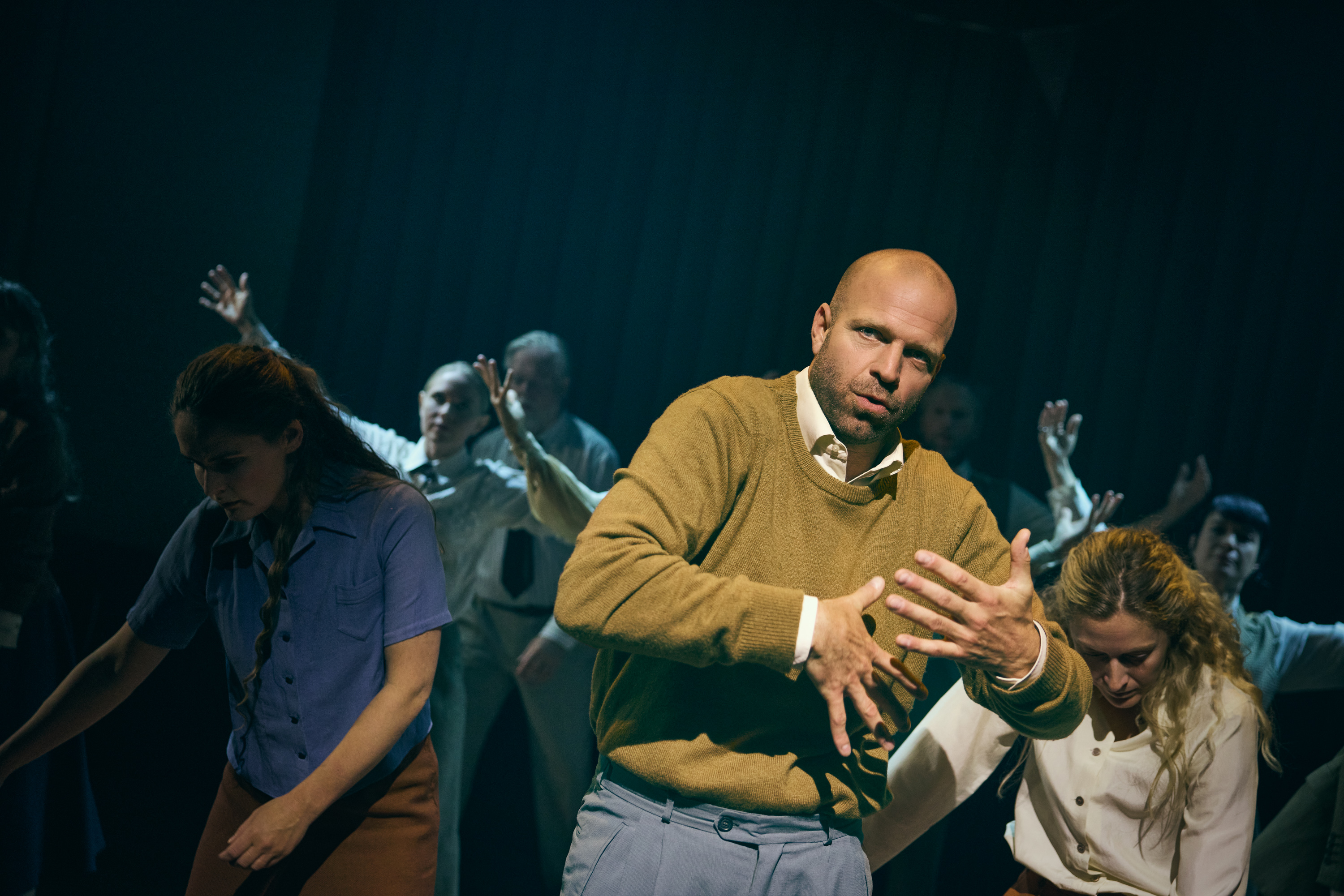 Skuespillere danser på scenen. En mand i striktrøje er i fokus. Fra forestillingen Alt i alt på Odense Teater