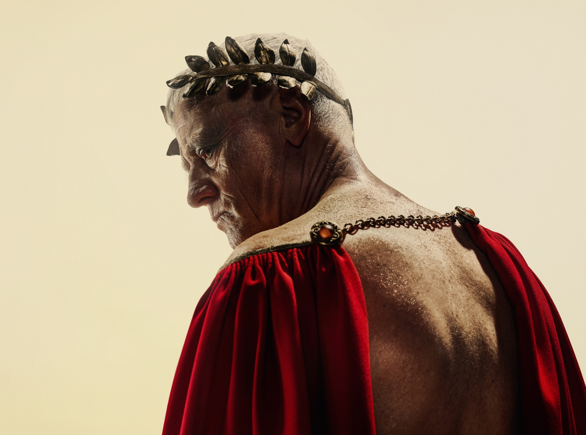 En mand iført rød kappe der blotter hans nøgne ryg og en gylden laurbærkrans på hovedet ser sig over skulderen. Fra forestilling Julius Cæsar på Odense Teater