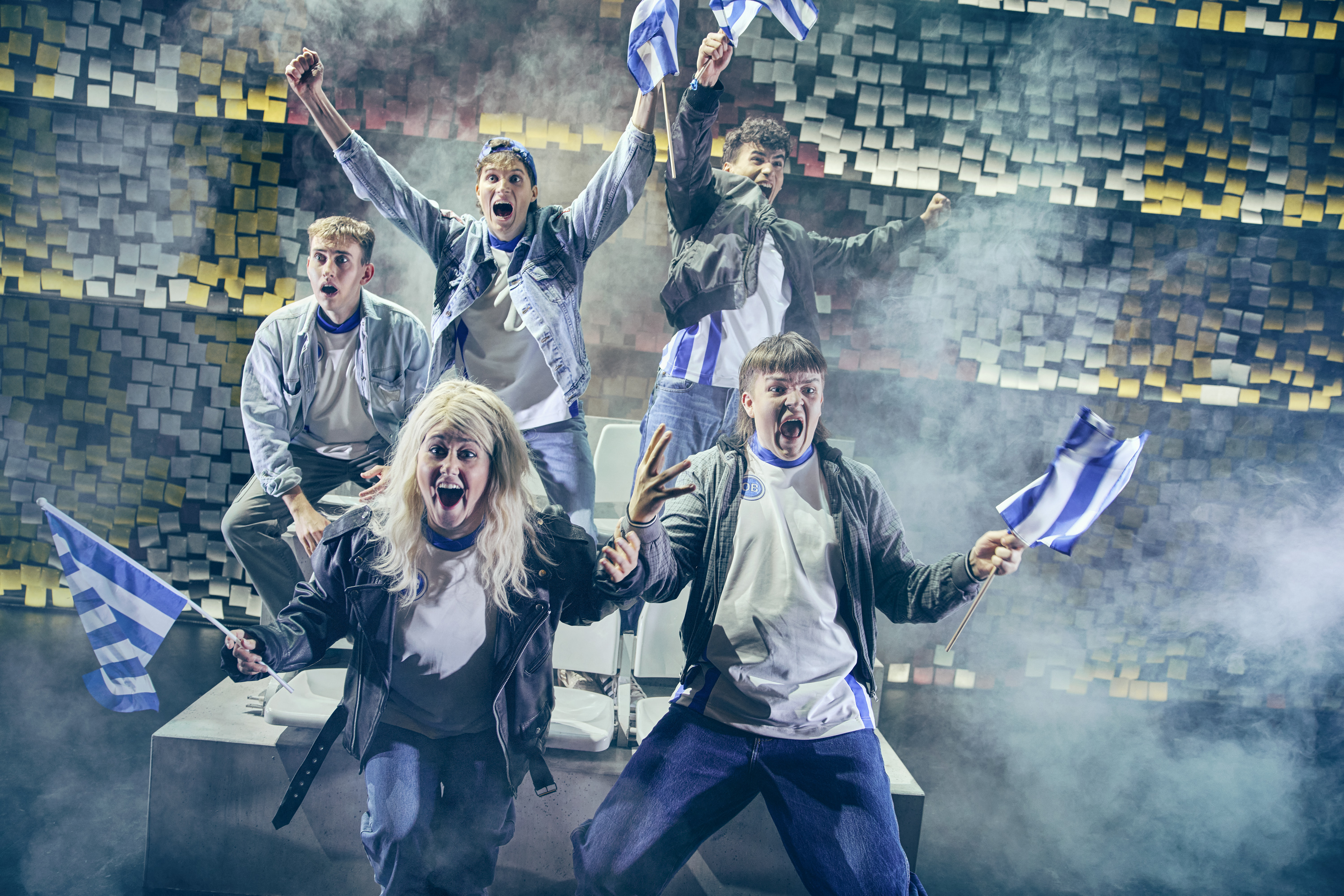 Fem unge mennesker jubler til med blå og hvidstribede flag. Fra teaterforestillingen Miraklet i Madrid på Odense Teater