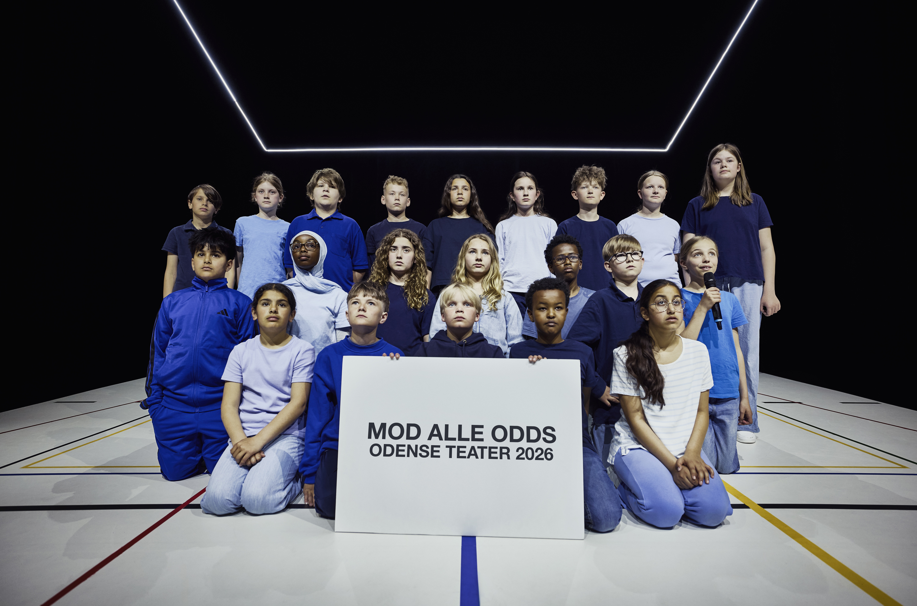 Gruppefoto af børn klædt i blåt tøj. De forreste holder stort skilt med teksten "Mod alle odds Odense Teater 2026"