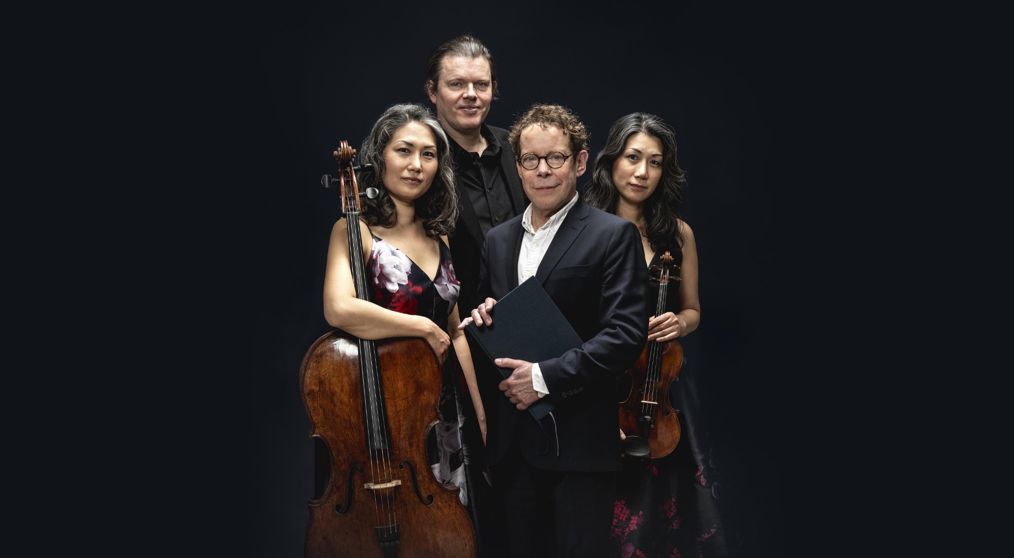 2 mænd og 2 kvinder med med cello og violin står tæt sammen- Sort baggrund. Fra forestillingen En digters bazar på Odense Teater