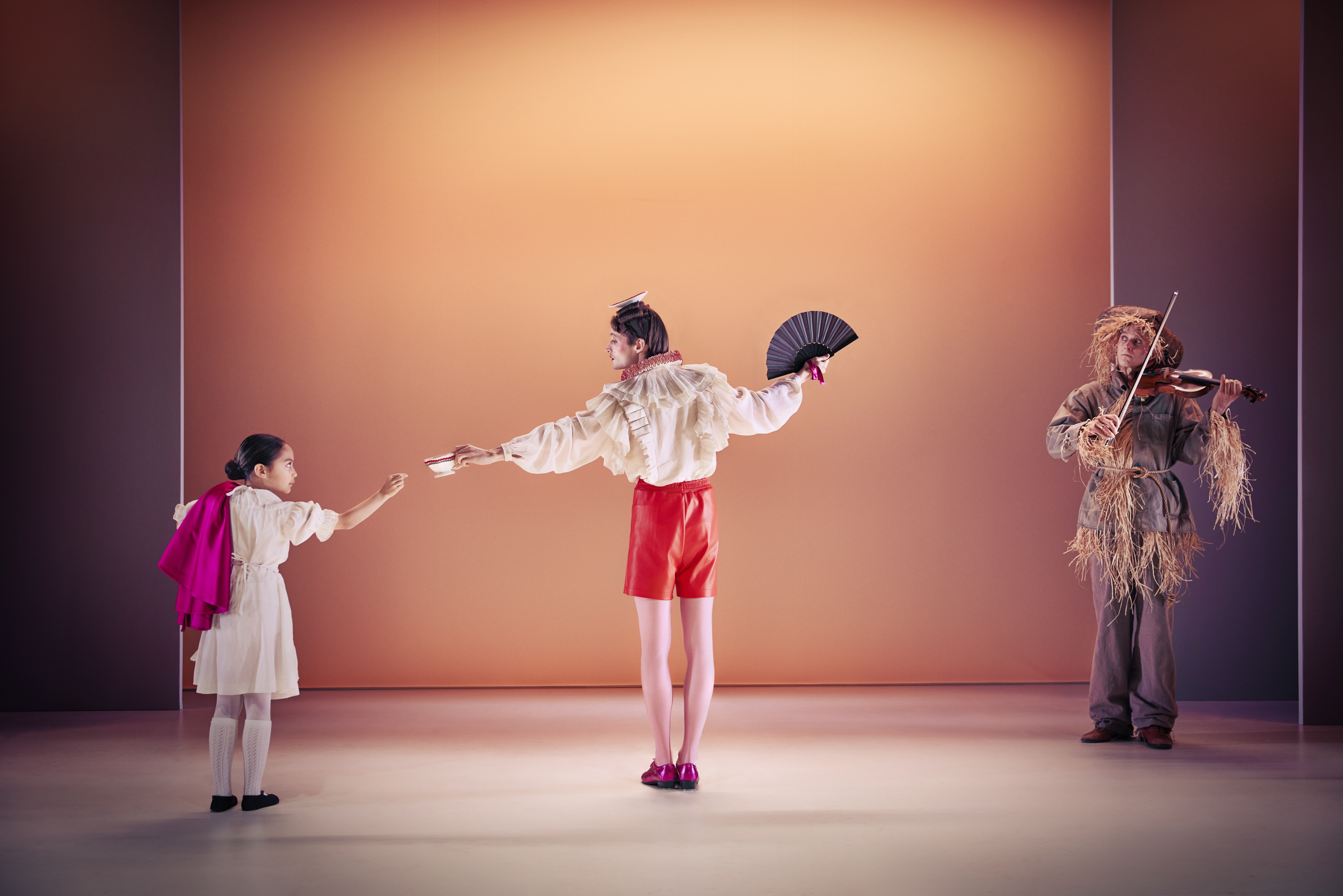 Den snobbede bror fra Klodshans med vifte på scenen med lille pige. I baggrund et fugleskræmsel der spiller violin. Fra Teaterforestilling Klodshans på Odense Teater