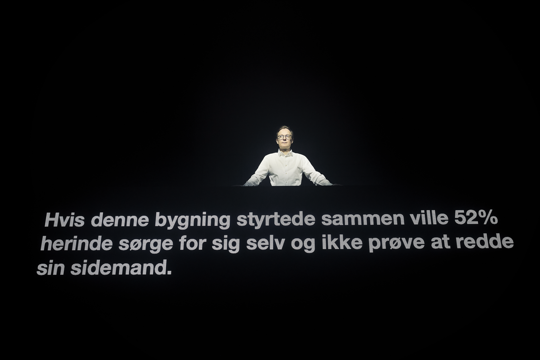 Sort billede med hvid tekst og en mand i hvid skjorte står ovenover teksten. Fra forestillingen AI know you på Odense Teater