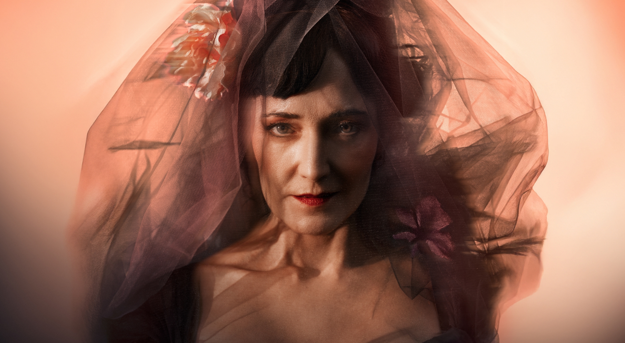 Portræt af mørkhåret kvinde med sort slør og en blomst i siden. Orange baggrund. Fra forestillingen Fru Marie Grubbe på Odense Teater