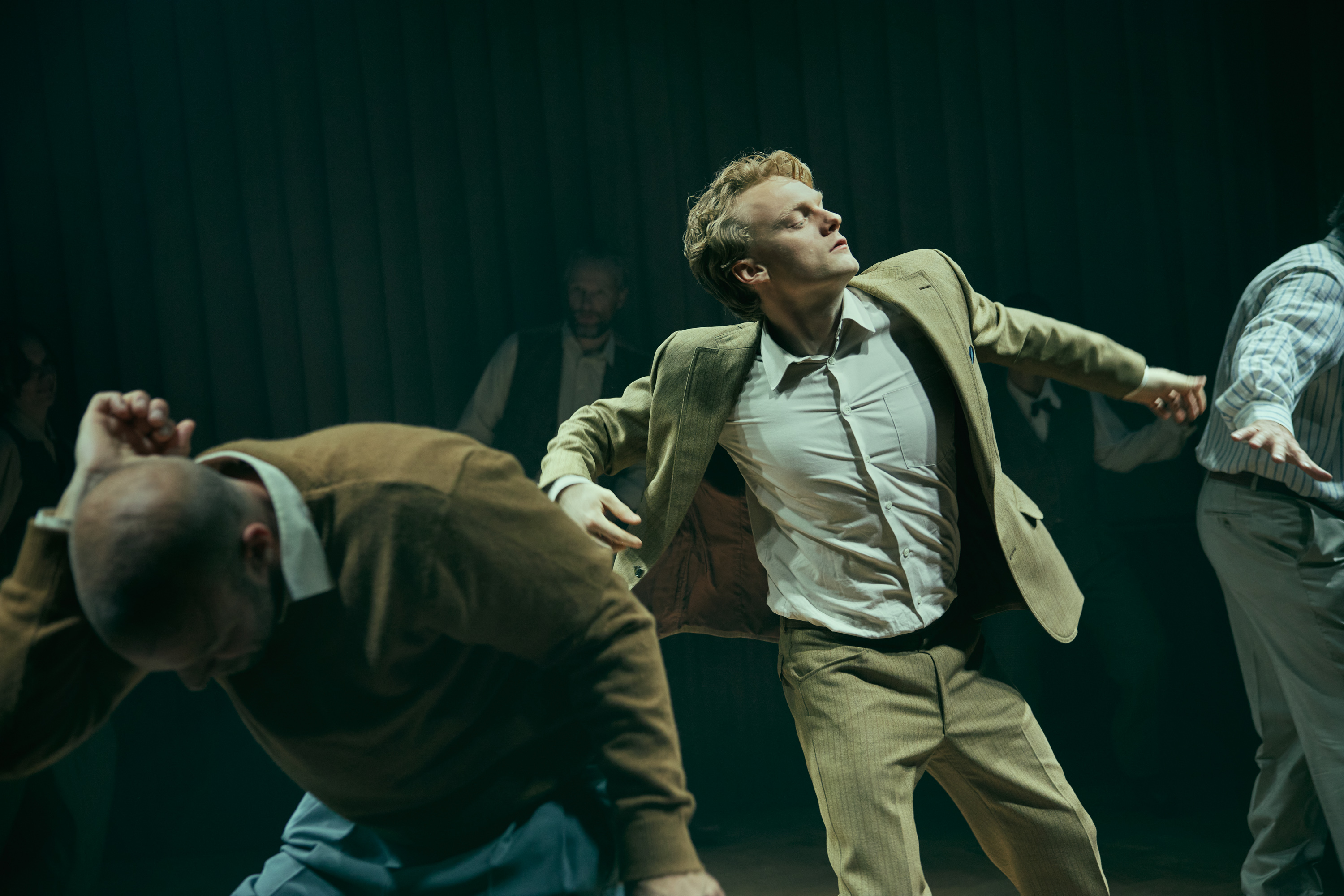 Skuespillere danser på scenen. En ung mand i lys habit er i fokus. Fra forestillingen Alt i alt på Odense Teater