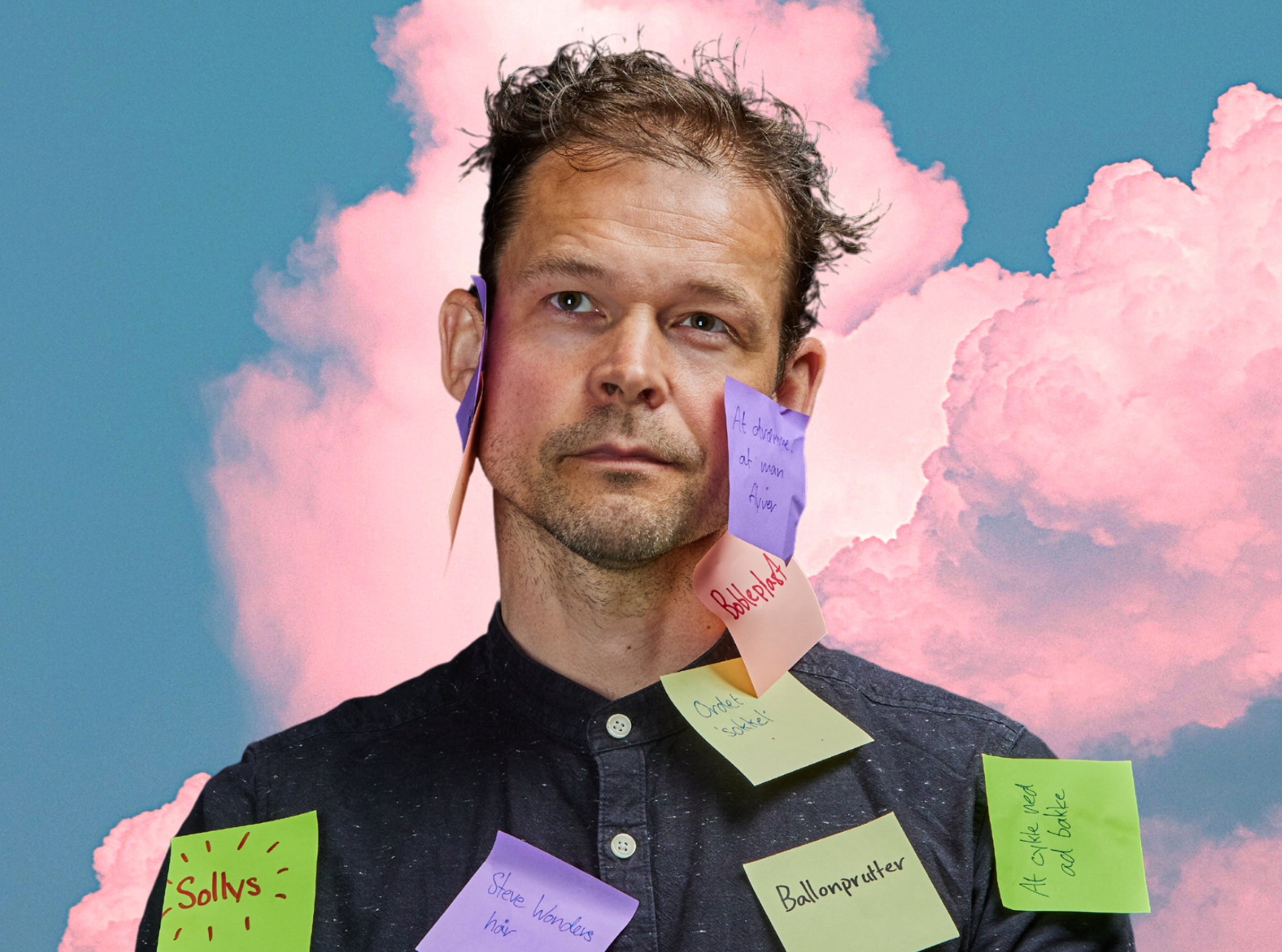 En mand i sort skjorte  med post-it noter klistret på skjorte og i ansigtet. Baggrund er blå himmel med lyserøde skyer. 
