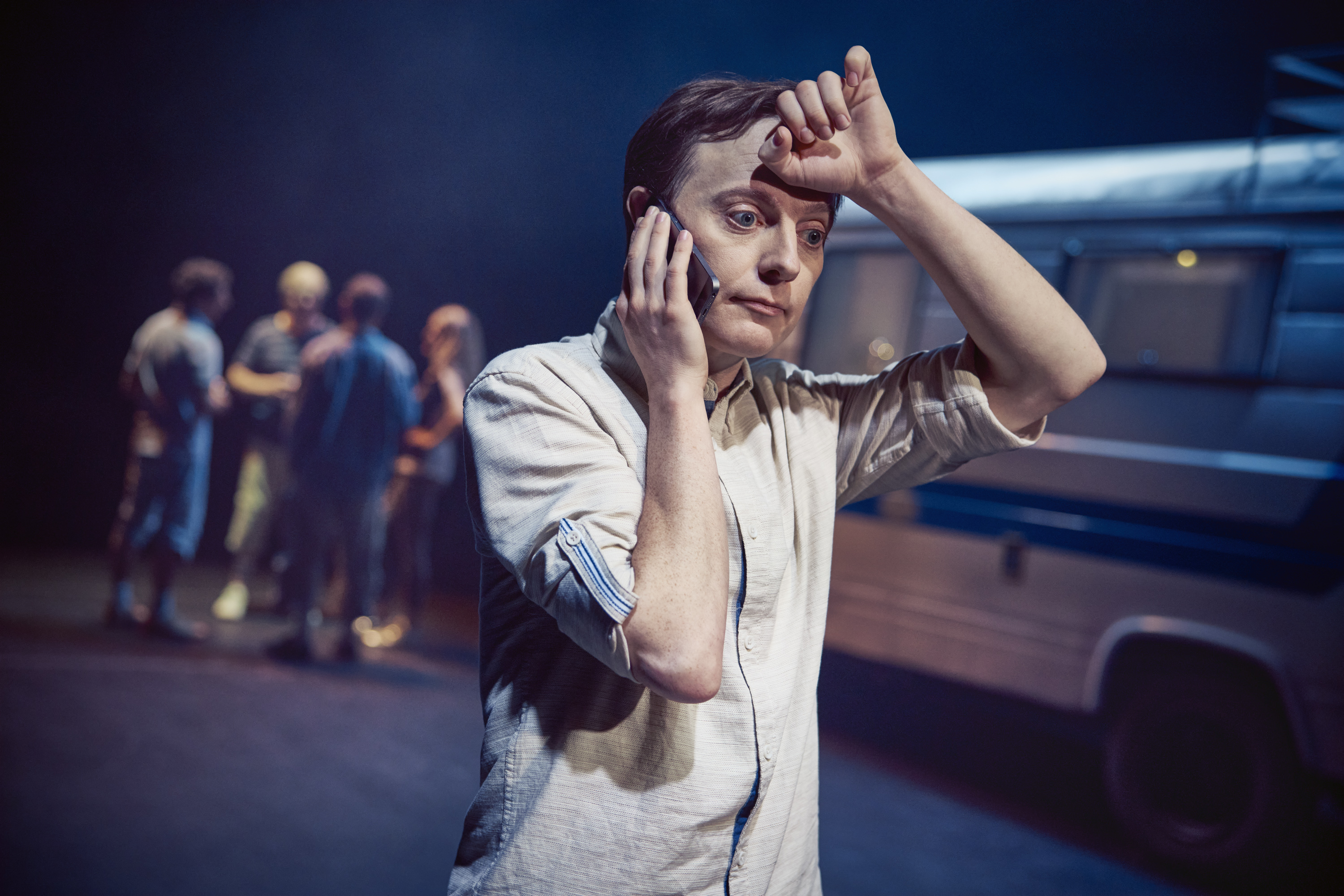 En yngre mand taler i telefon. Har et opgivende udtryk. Står foran gammel autocamper. Fra teaterforestillingen Miraklet i Madrid på Odense Teater