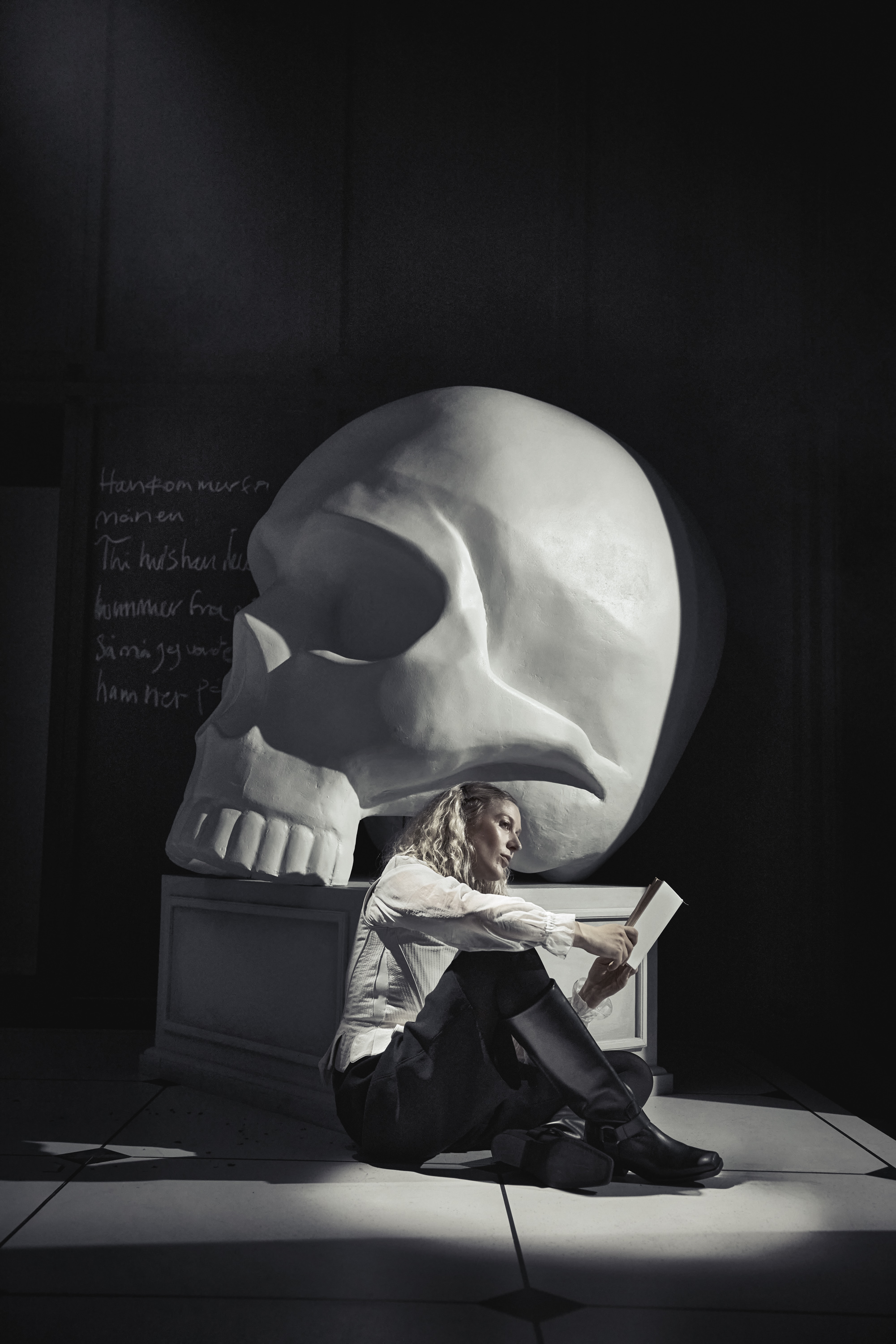 Kvinde sidder lænet op af podie med stort hvidt kranium. Fra forestilling Cyrano de Bergerac på Odense Teater