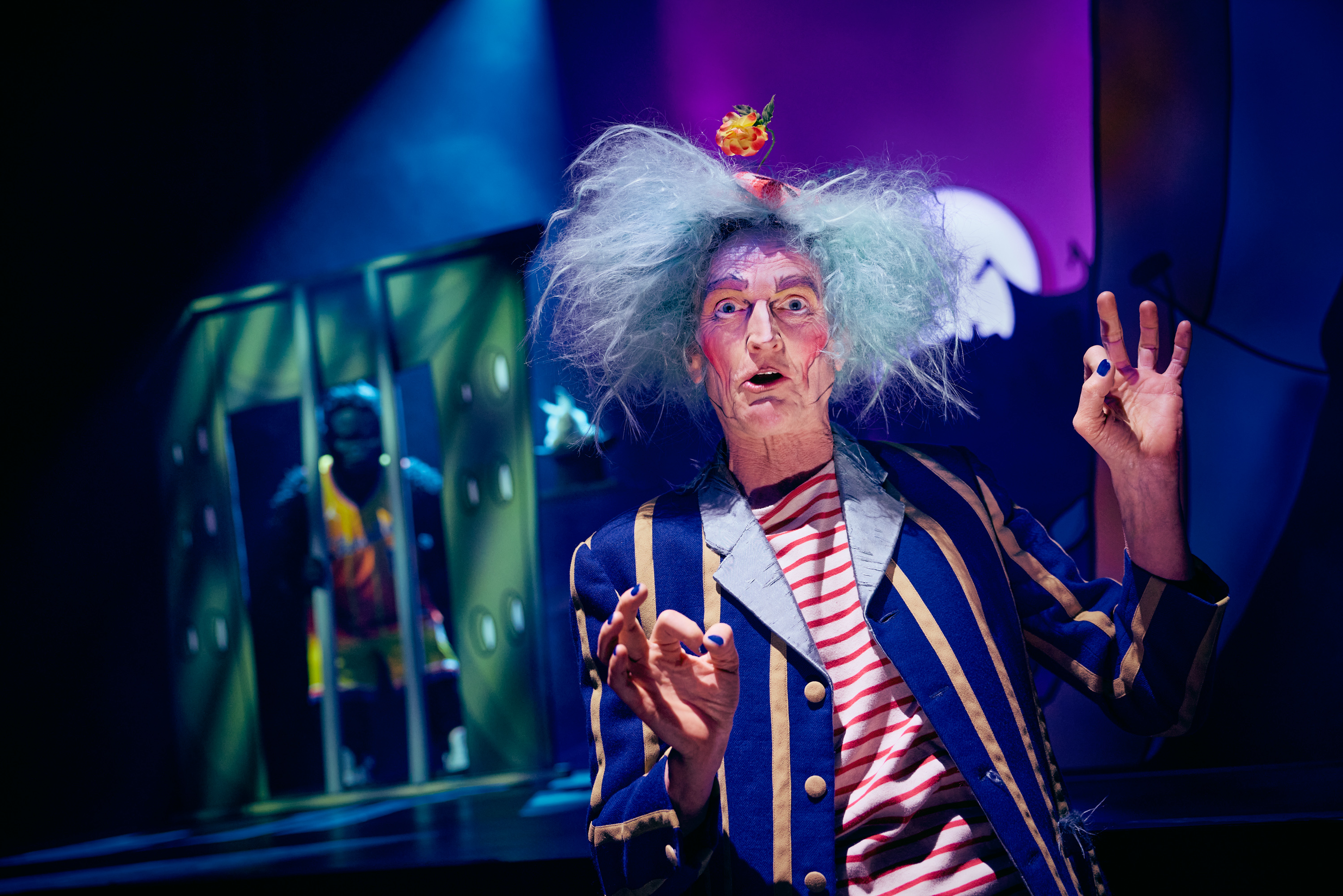 En mand i stribet tøj og vildt gråt hår. I baggrunden en gorilla i bur. Fra forestillingen Håndbog for superhelte på Odense Teater