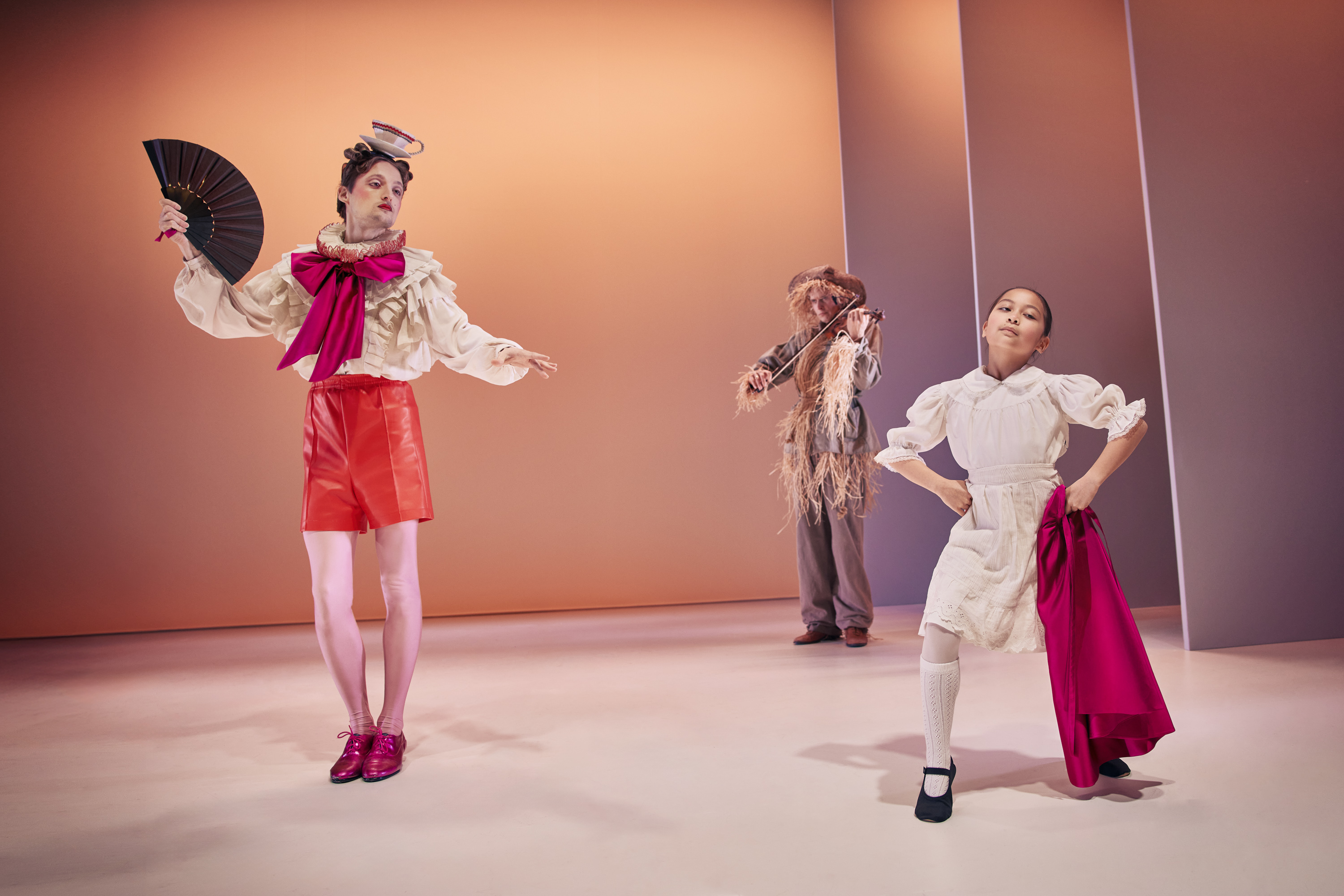 Den snobbede bror fra Klodshans med vifte på scenen med lille pige. I baggrund et fugleskræmsel der spiller violin. Fra Teaterforestilling Klodshans på Odense Teater