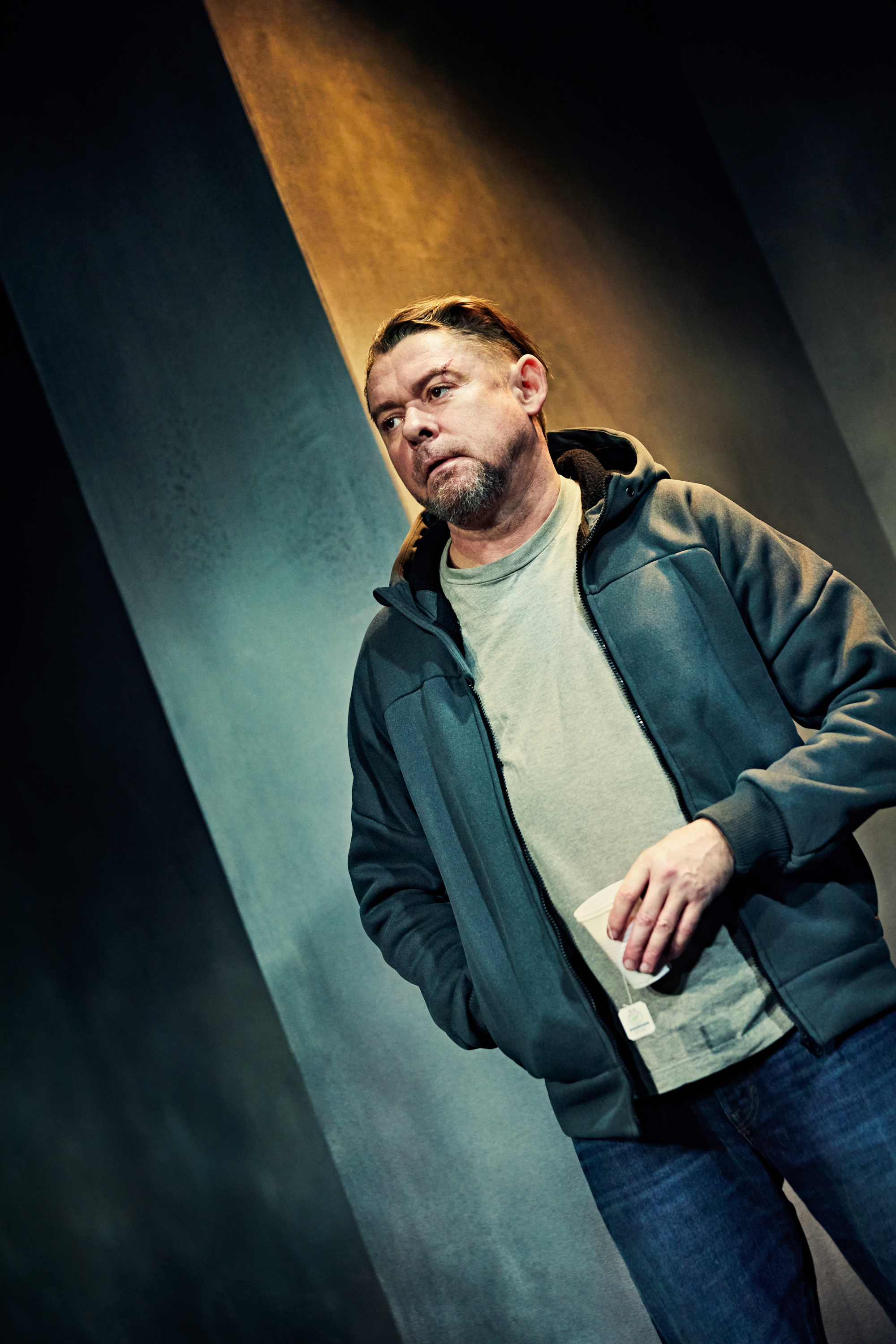 Mand står med plastikkop med tebrev. Fra forestilling Maria på Odense Teater.