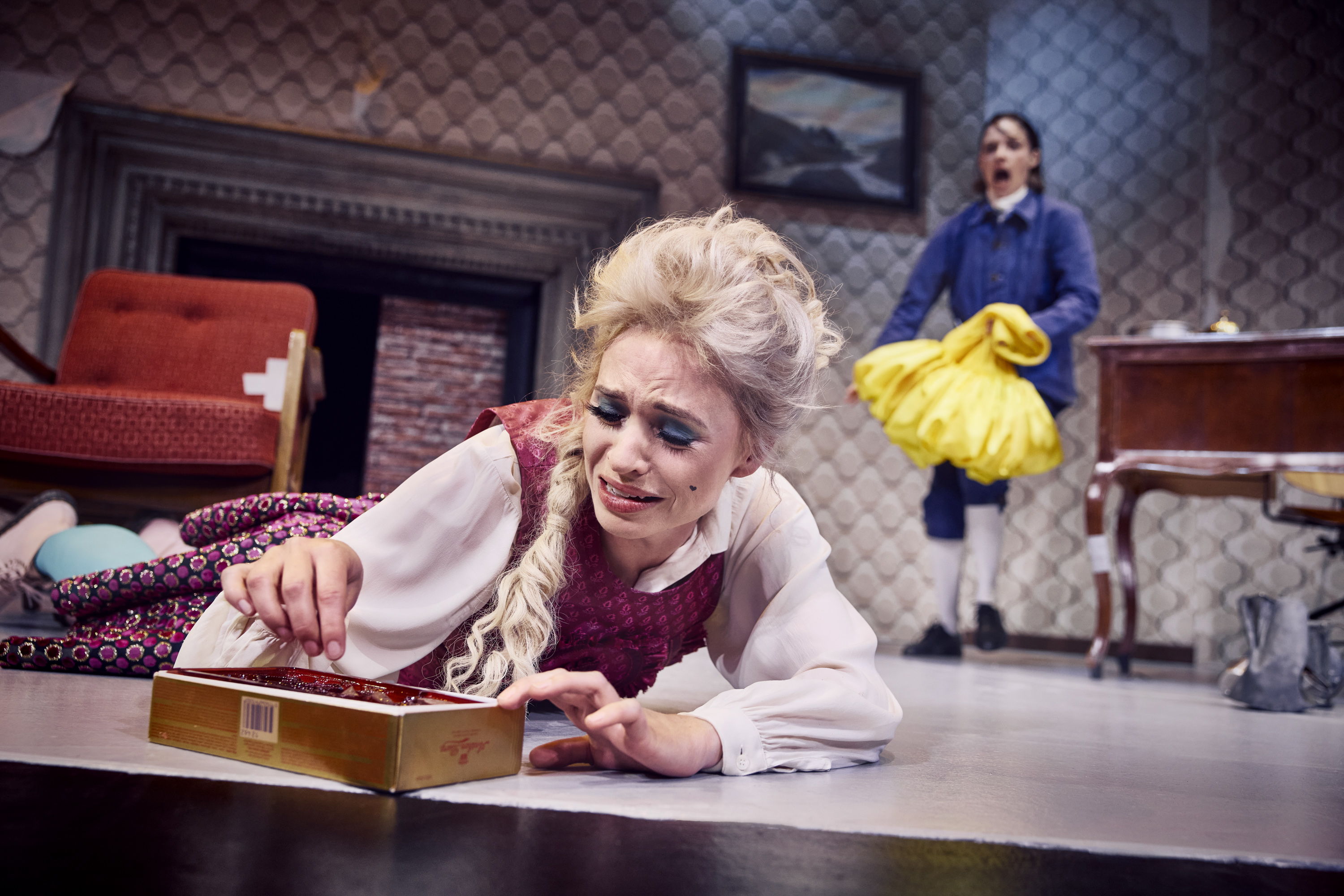 En kvinde ligger på et gulv. Hun græder mens hun spiser chokolade direkte fra æsken. Fra teaterforestillingen Den politiske kandestøber på Odense Teater