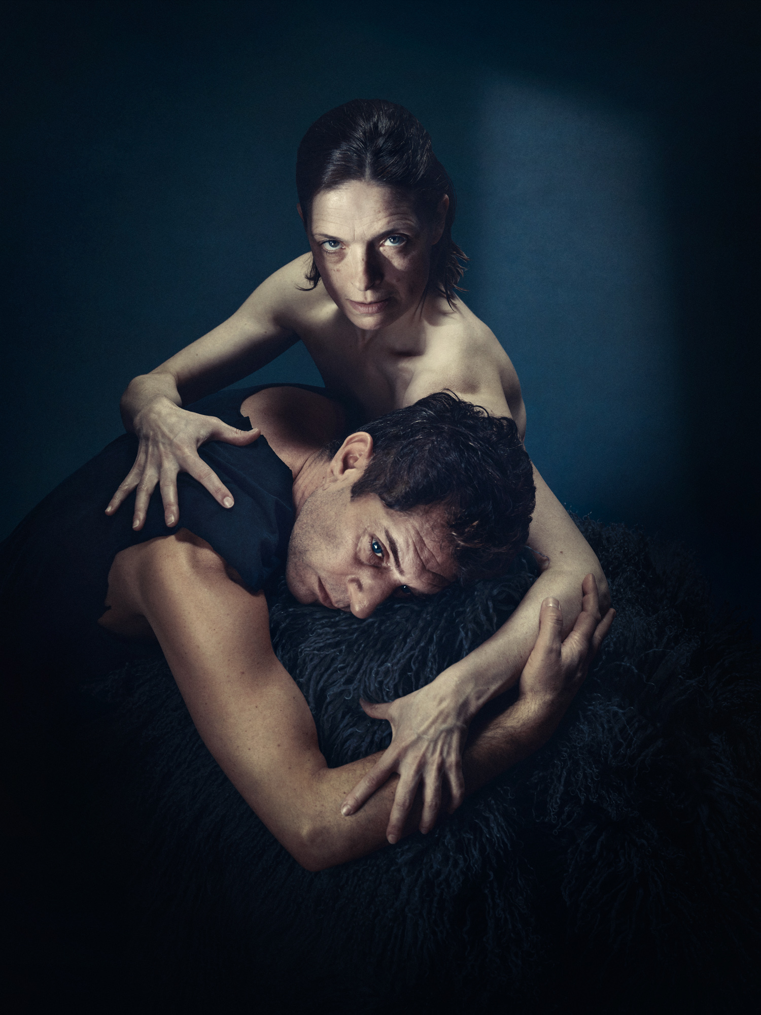 En kvinde med nøgen overkrop stirrer vagtsomt i kameraet, på hendes skød ligger en mørkhåret mand . Han ser ikke i kamera. Fra forestillingen Når vi døde vågner på Odense Teater