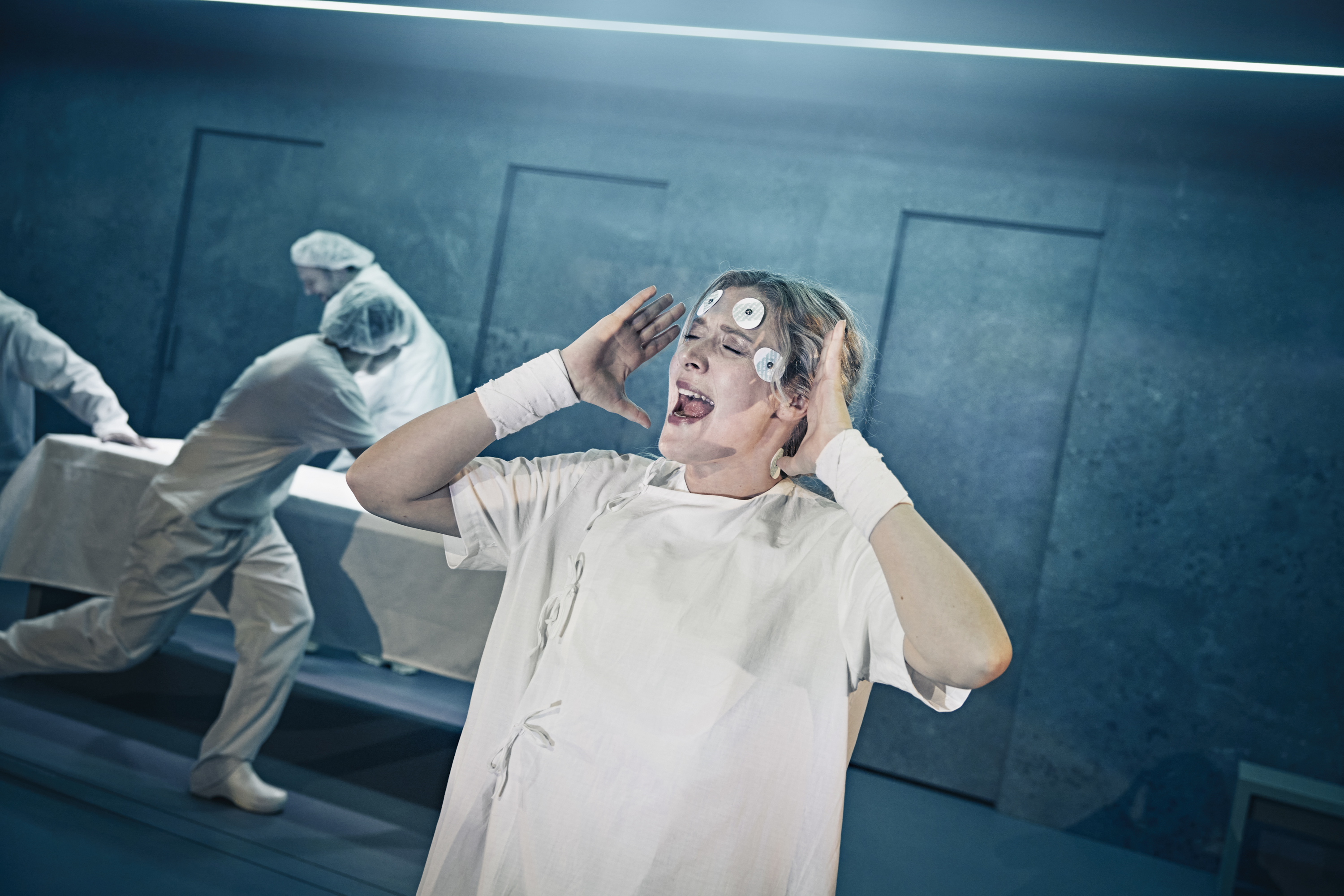 En kvinde i hospitalstøj med elektroder i panden skriger i musicalen Next to Normal på Odense Teater