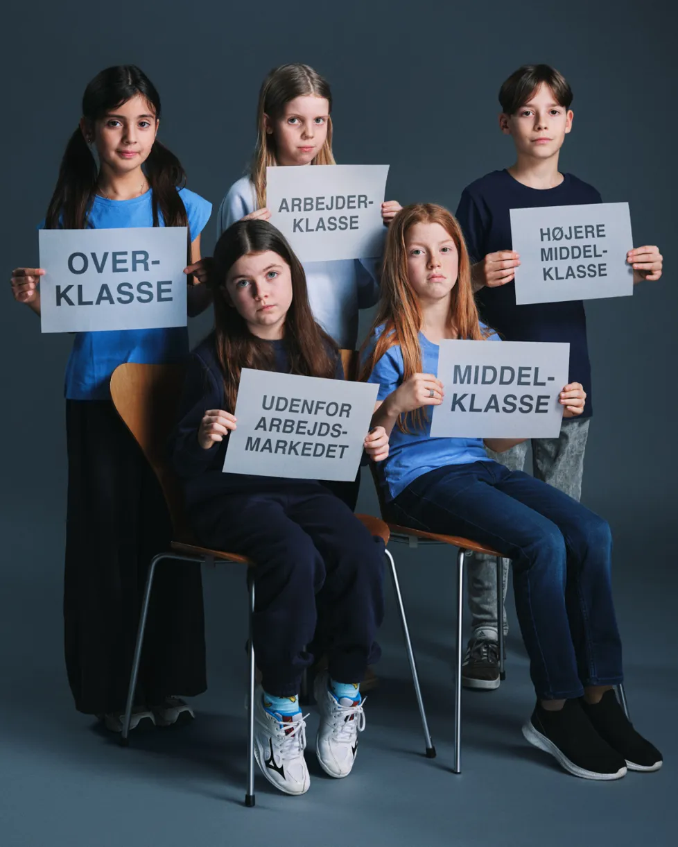 fem børn klædt i blåt. 2 sidder og 3 står. De holder hvide skilte med sort skrift. Fra forestilling Mod alle ods på Odense Teater