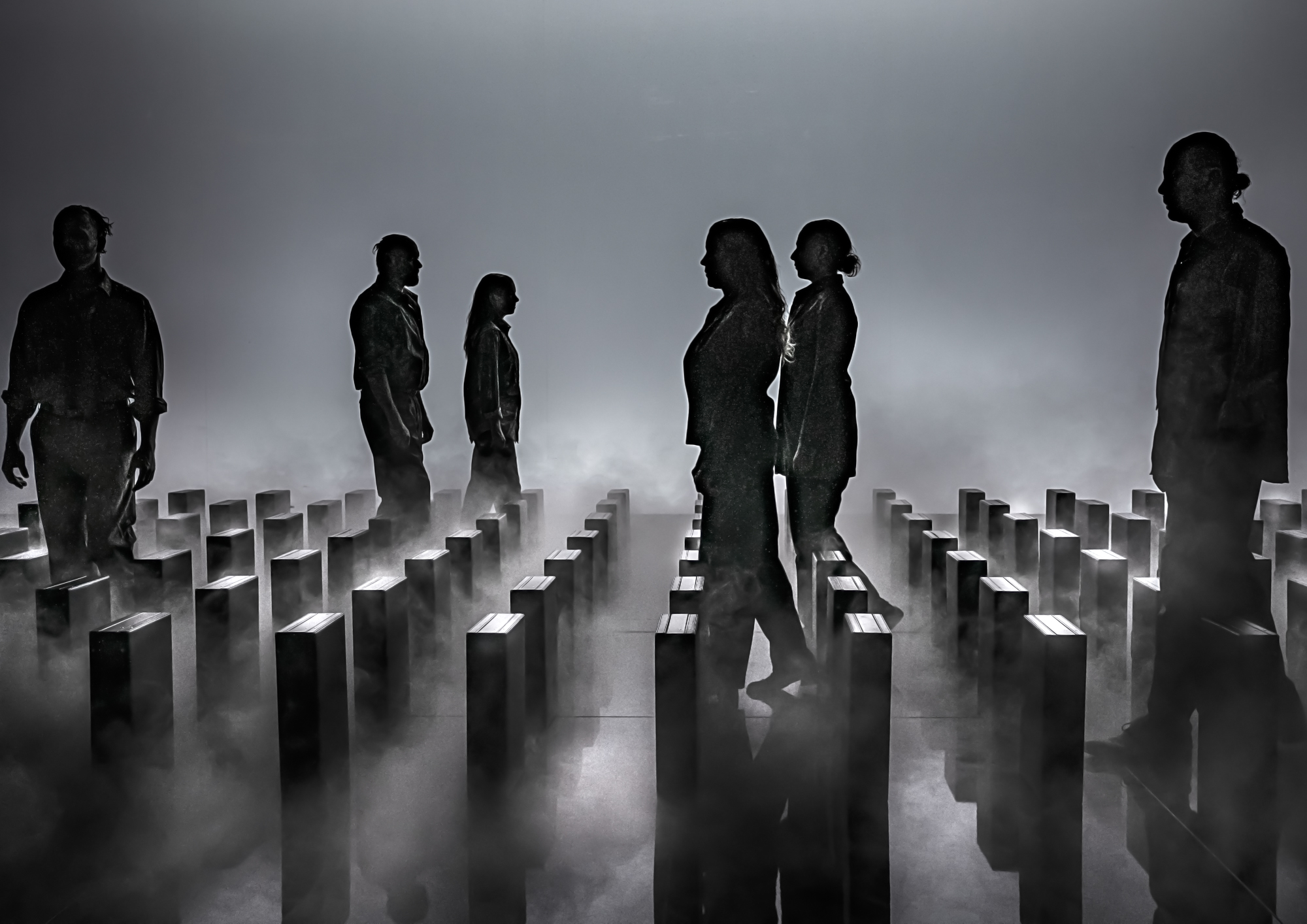 6 personer i gråt beskidt tøj går i mellem hvad der ligner gravsten på række, som på amerikansk kirkegår. Røg og gråt lys. 