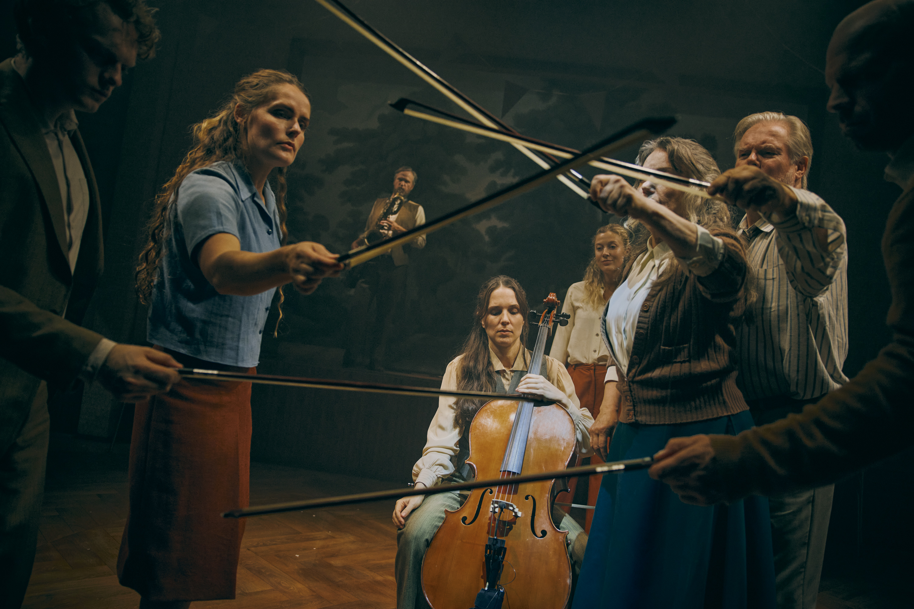 Flere mennesker på en scene står med violinbuer løftet op. i bagrund sidder en kvindelig musiker med en cello. Fra forestillingen Alt i alt på Odense Teater