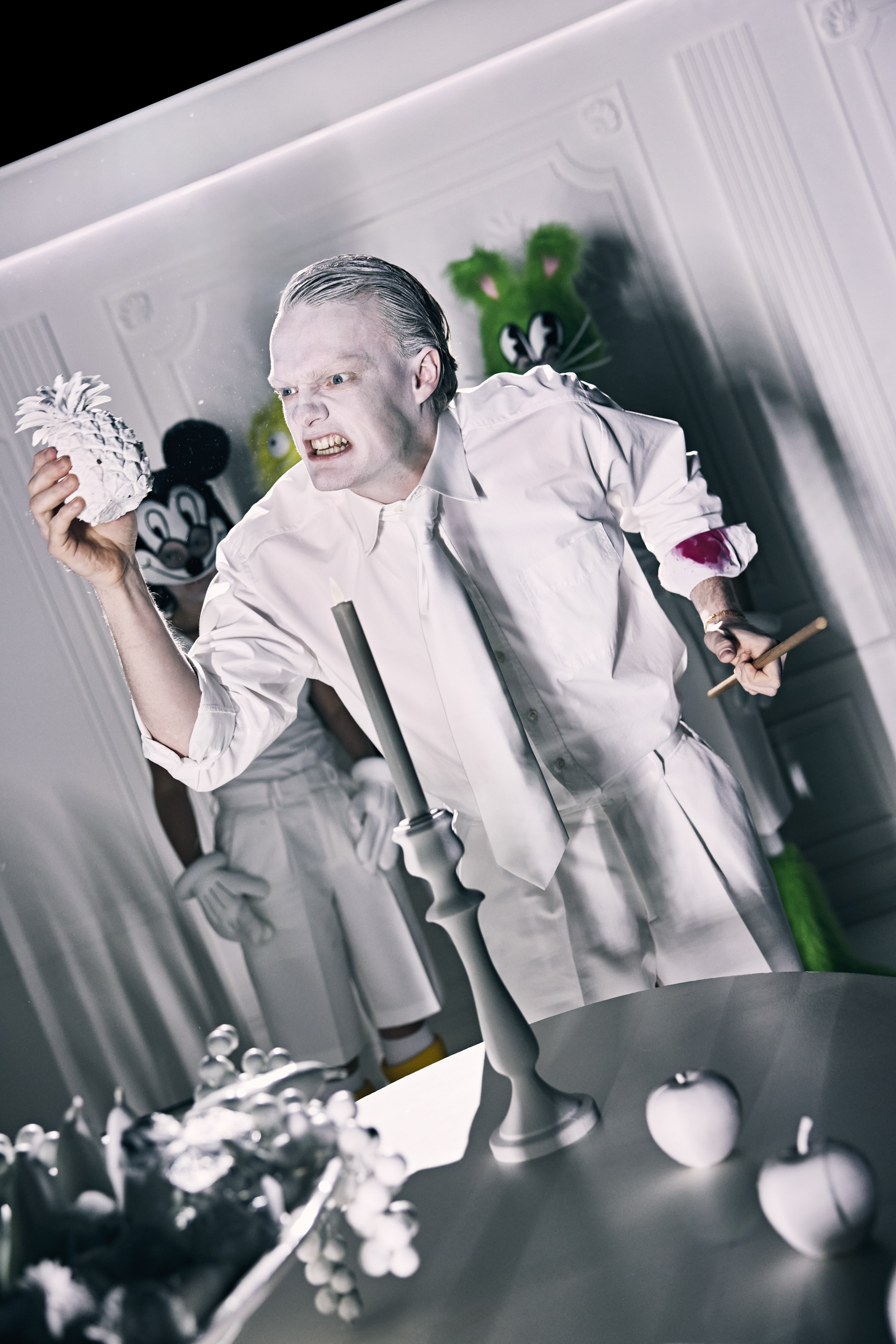 Mand klædt i hvidt. Ser vredt på en hvid ananas han holder op foran ansigtet. Fra forestilling Resten kender du fra film på Odense Teater