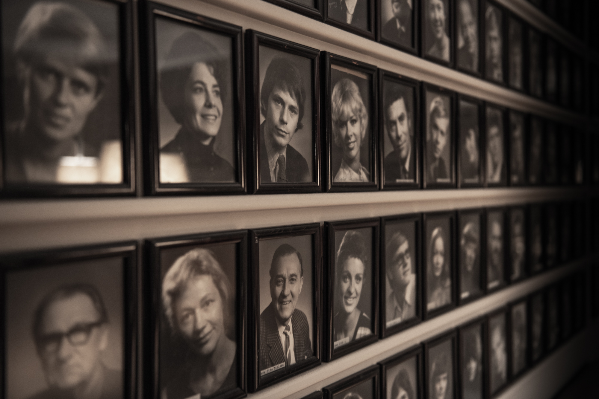 Gamle sort-hvide portrætbilleder af tidligere skuespillere på Odense Teater i mørke rammer på væg