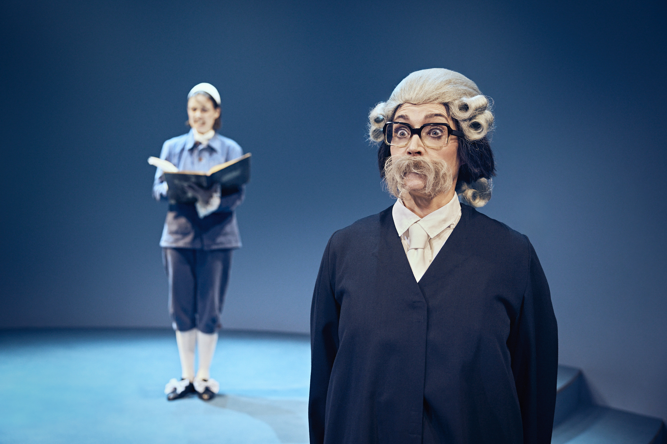 to mennesker på en scene. Den forreste med stort hvalros skæg, briller og paryk fra 1700 tallet. Fra teaterforestillingen Den politiske kandestøber på Odense Teater