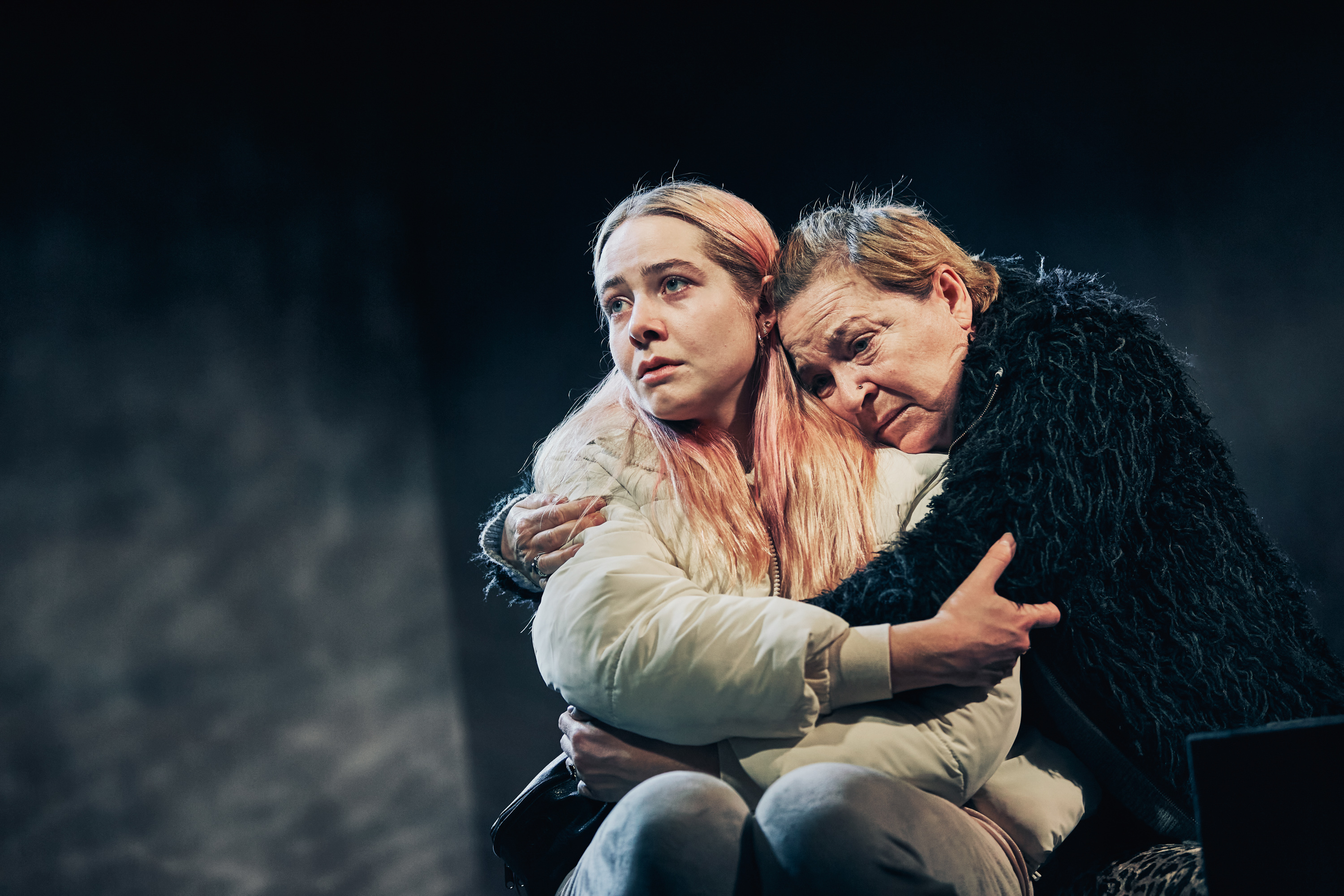 En kvinde i sort pelsjakke knuger en yngre kvinde ind til sig. Fra forestilling Maria på Odense Teater