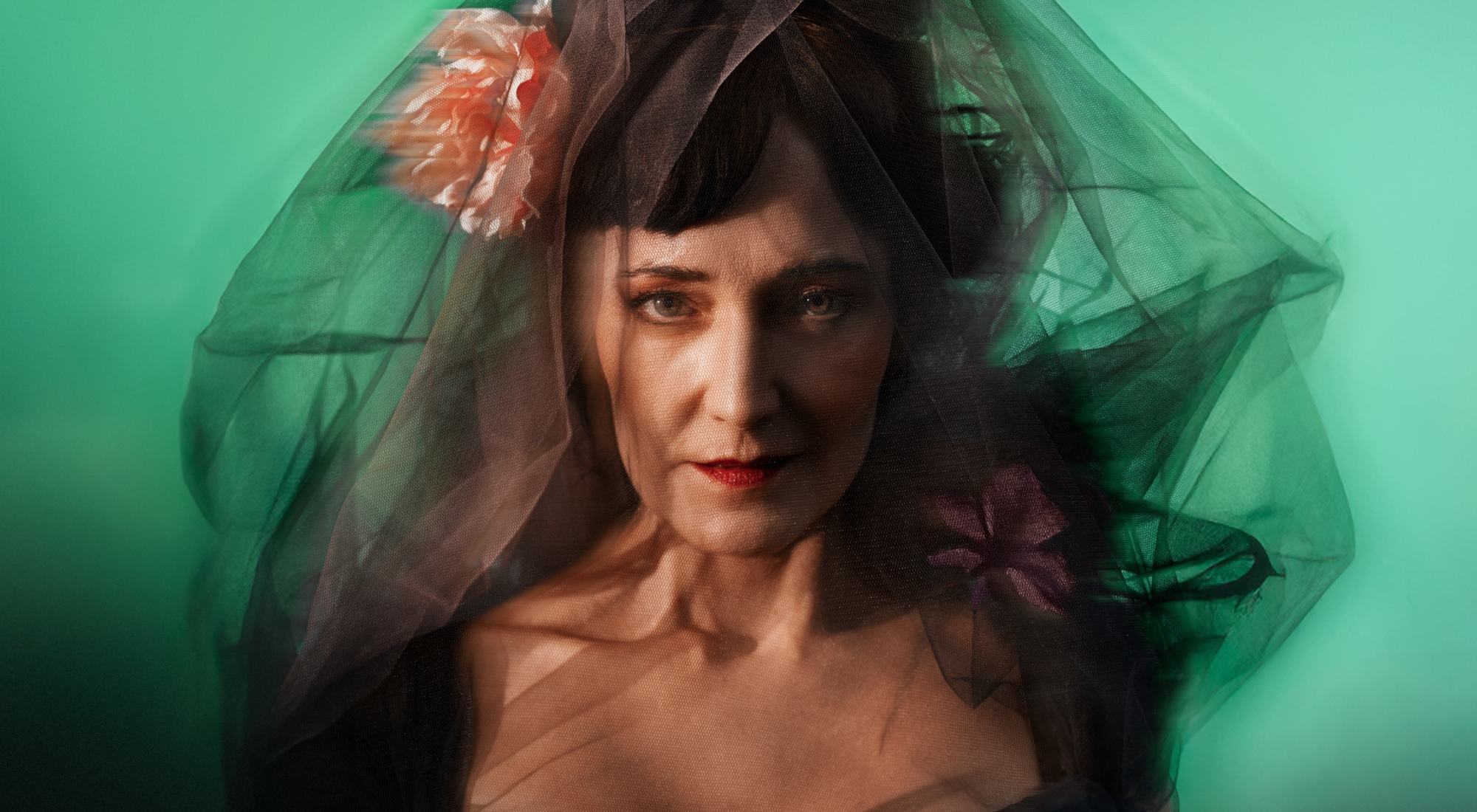 Portræt af mørkhåret kvinde med sort slør og en blomst i siden. Grøn baggrund. Fra forestillingen Fru Marie Grubbe på Odense Teater