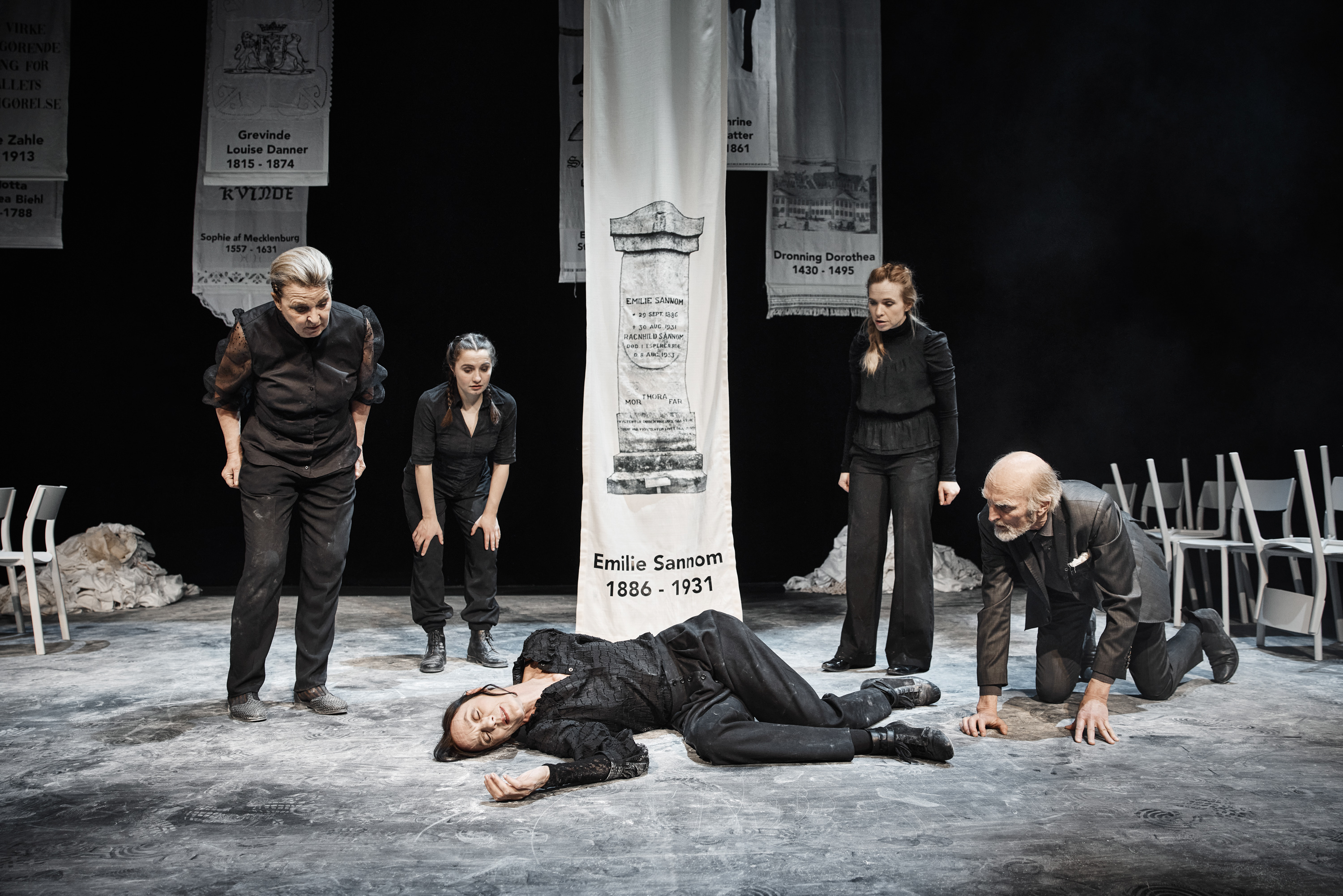 En kvinde er faldet om på støvet gulv. Tre kvinder og en mand ser undersøgende på hende. Fra forestilling Kvinde kend din historie på Odense Teater