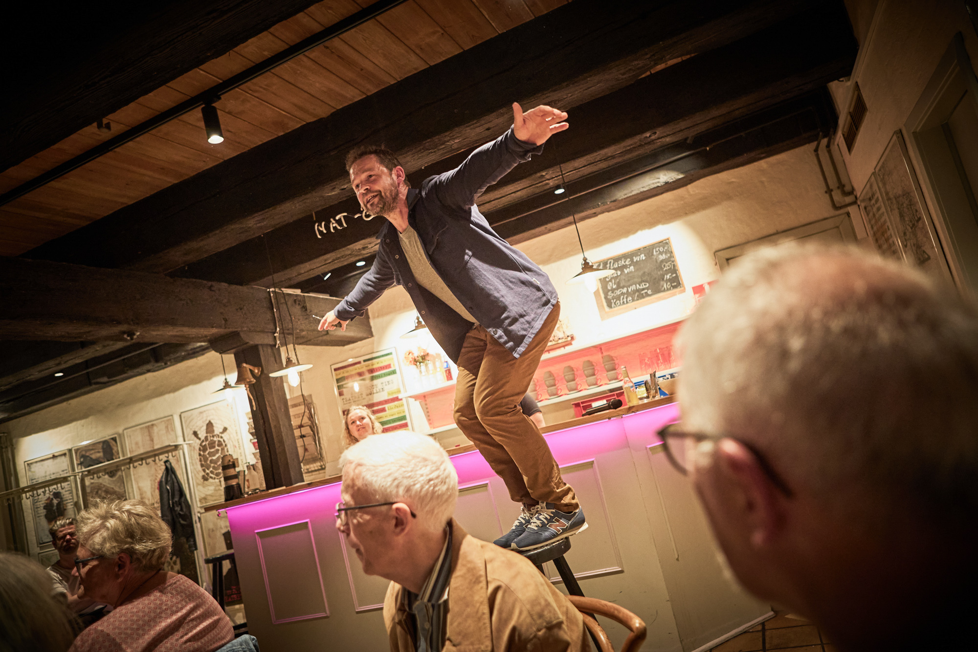 Mand står på barstol i lokale hvor andre lytter til hvad han siger