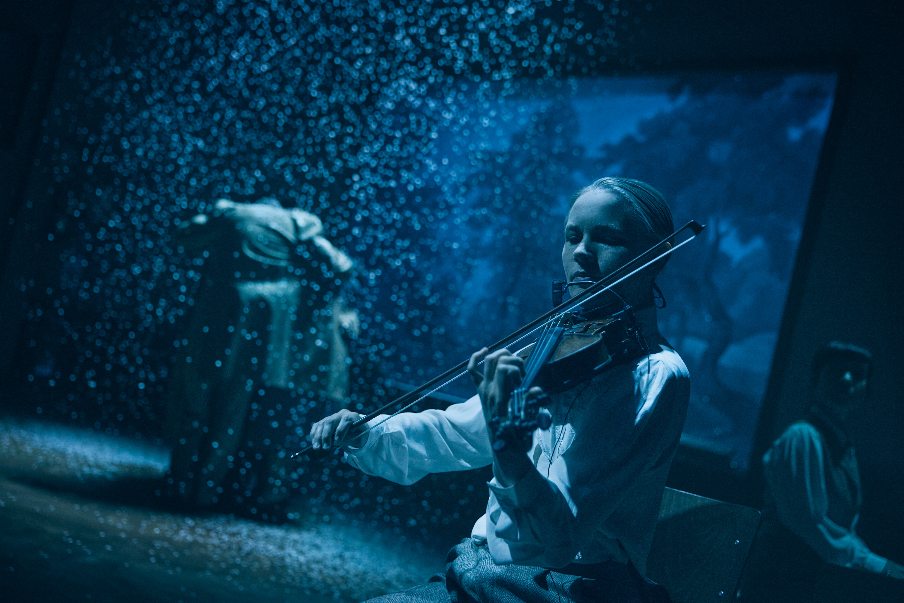 En ung kvinde spiller violin. I baggrunden er det mørkt og der er sne. Fra forestillingen Alt i alt på Odense Teater