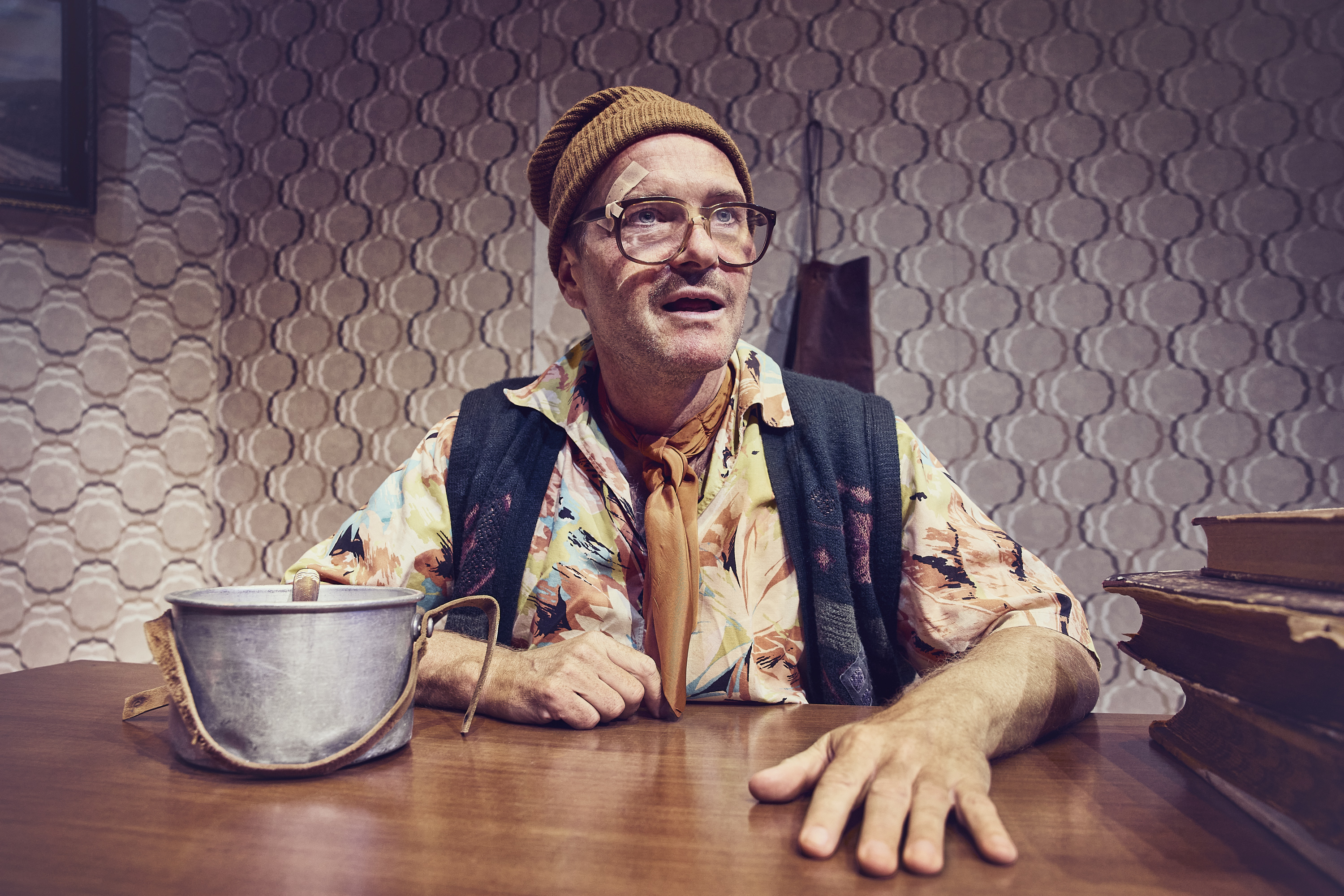 En mand med strikhue og store briller sidder ved et skrivebord. Fra teaterforestillingen Den politiske kandestøber på Odense Teater