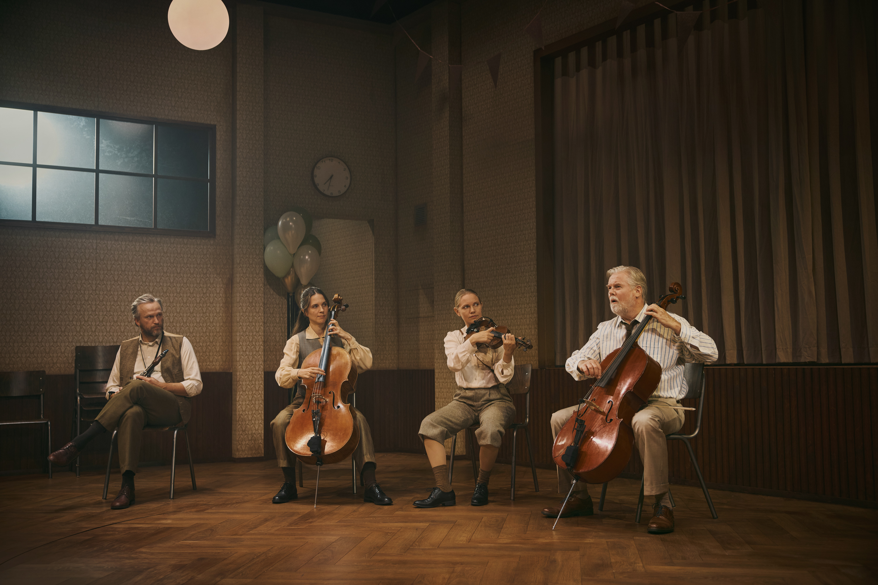 Fire musiker i et forsamlingshus. De har hhv. cello, violin og klarinet. Fra forestillingen Alt i alt på Odense Teater